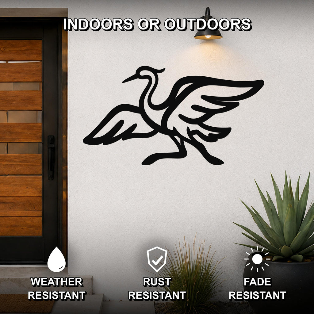 Black metal crane wall art silhouette with extended wings and long legs, mounted on a white exterior wall beside a wooden door and potted plants.