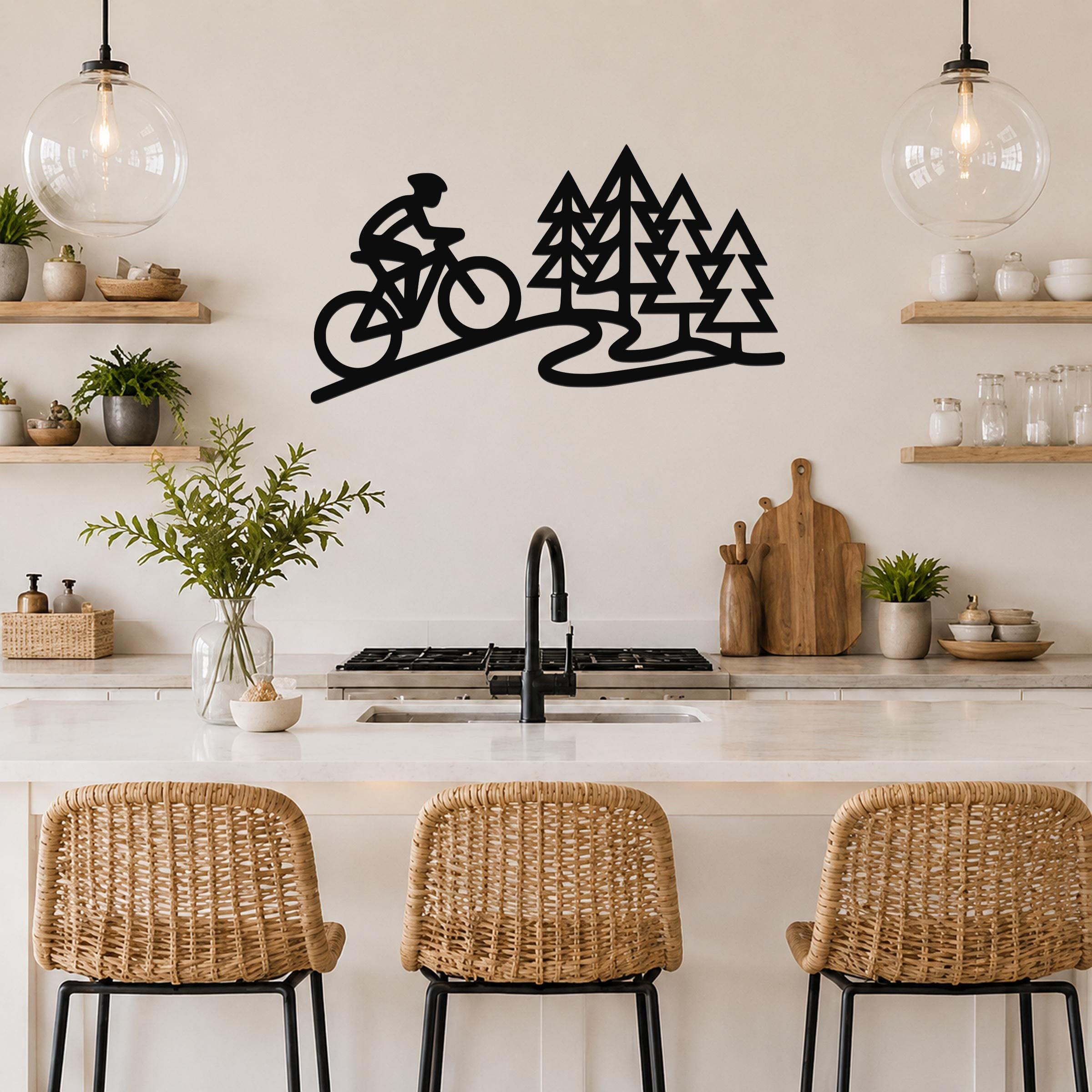 Black metal wall art silhouette of a cyclist on a trail with pine trees, mounted above a kitchen counter.