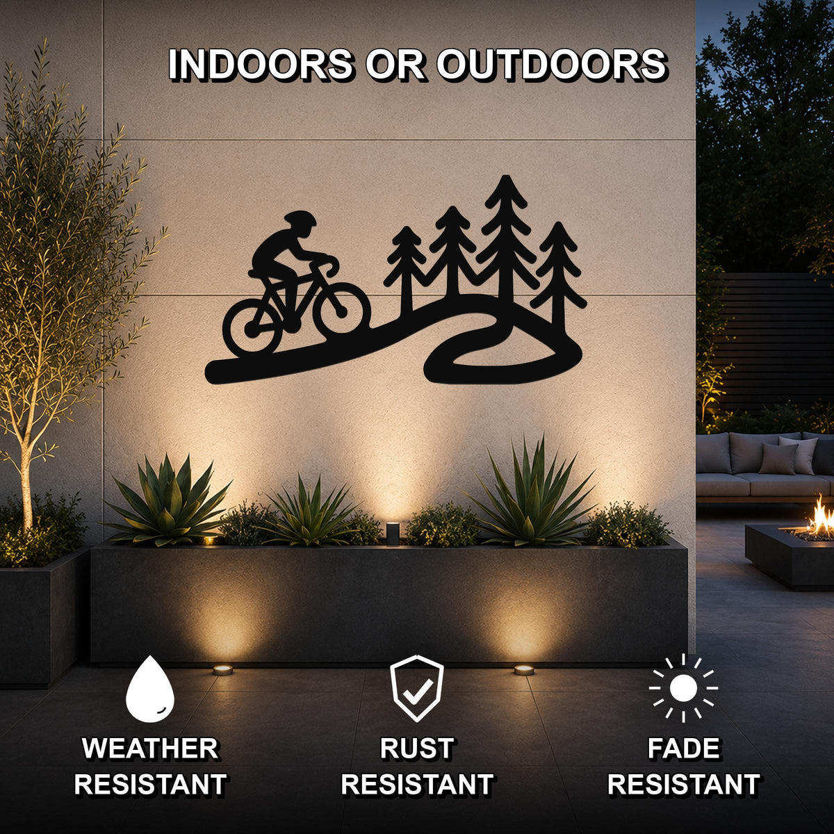 Black metal wall art featuring a cyclist silhouette on a winding path with pine trees, mounted on an outdoor wall above a planter in a patio setting.
