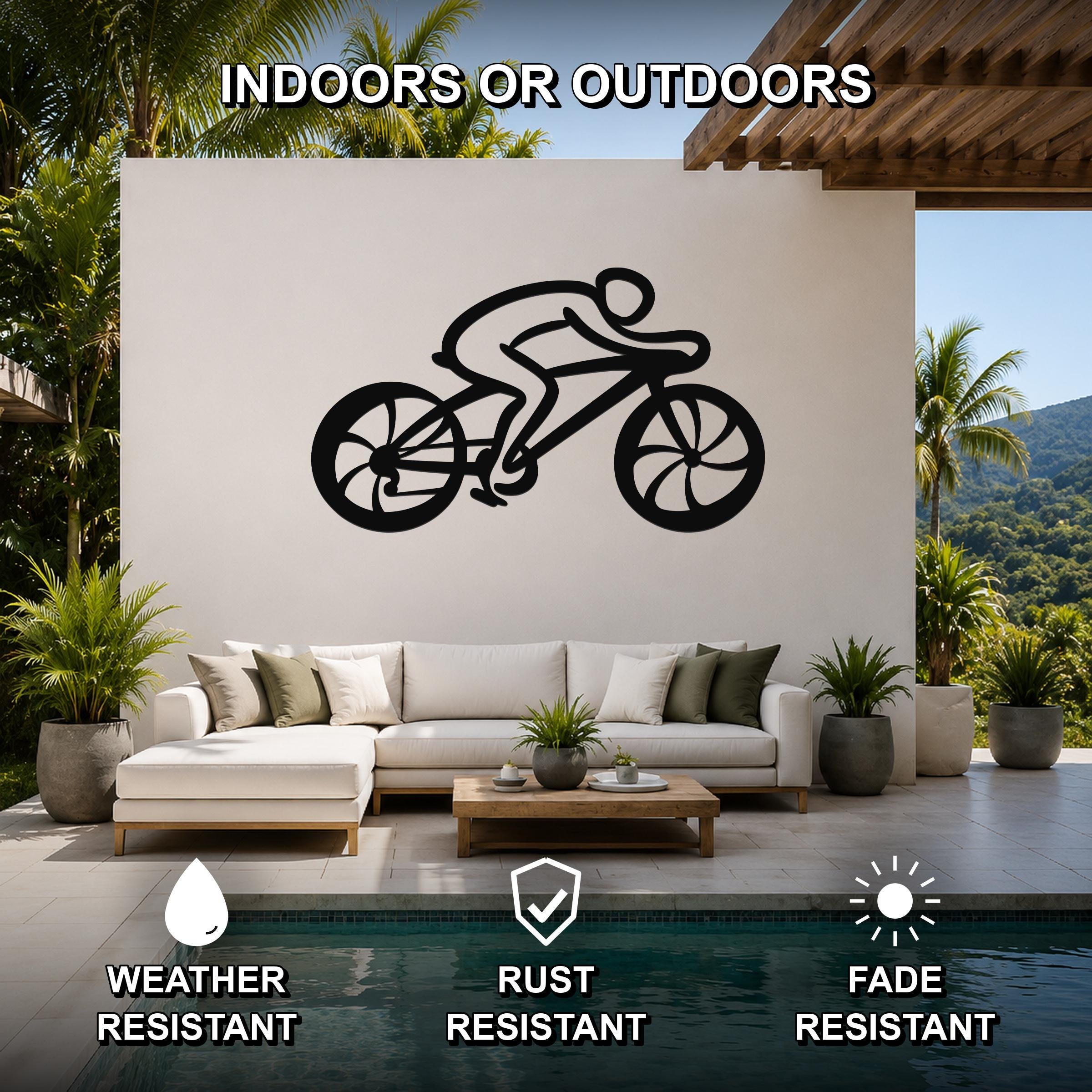 Black metal cycling wall art with a rider silhouette and wheel cutouts, mounted on a white outdoor wall above a sofa in a patio living area.