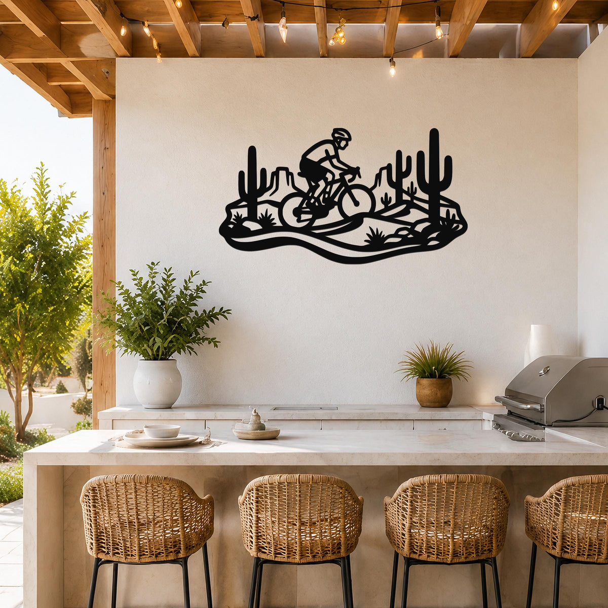 Black metal wall art silhouette of a cyclist on a mountain bike through a Sonoran desert landscape with saguaro cacti, mounted on a white wall above a kitchen counter.