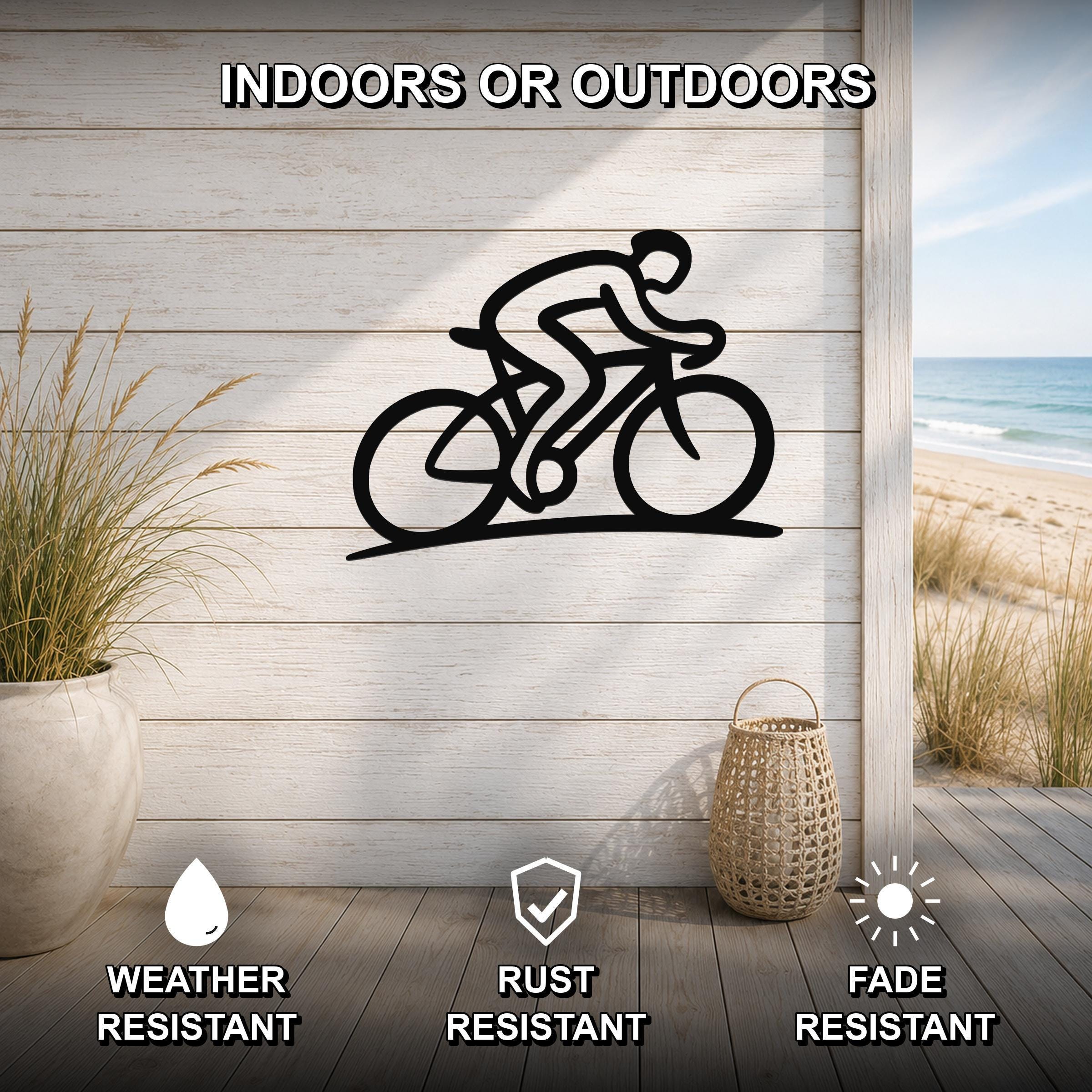 Black metal wall art featuring a cyclist silhouette in motion, mounted on a light wood-paneled wall above a deck with a beach view, weather, rust, and fade resistant.