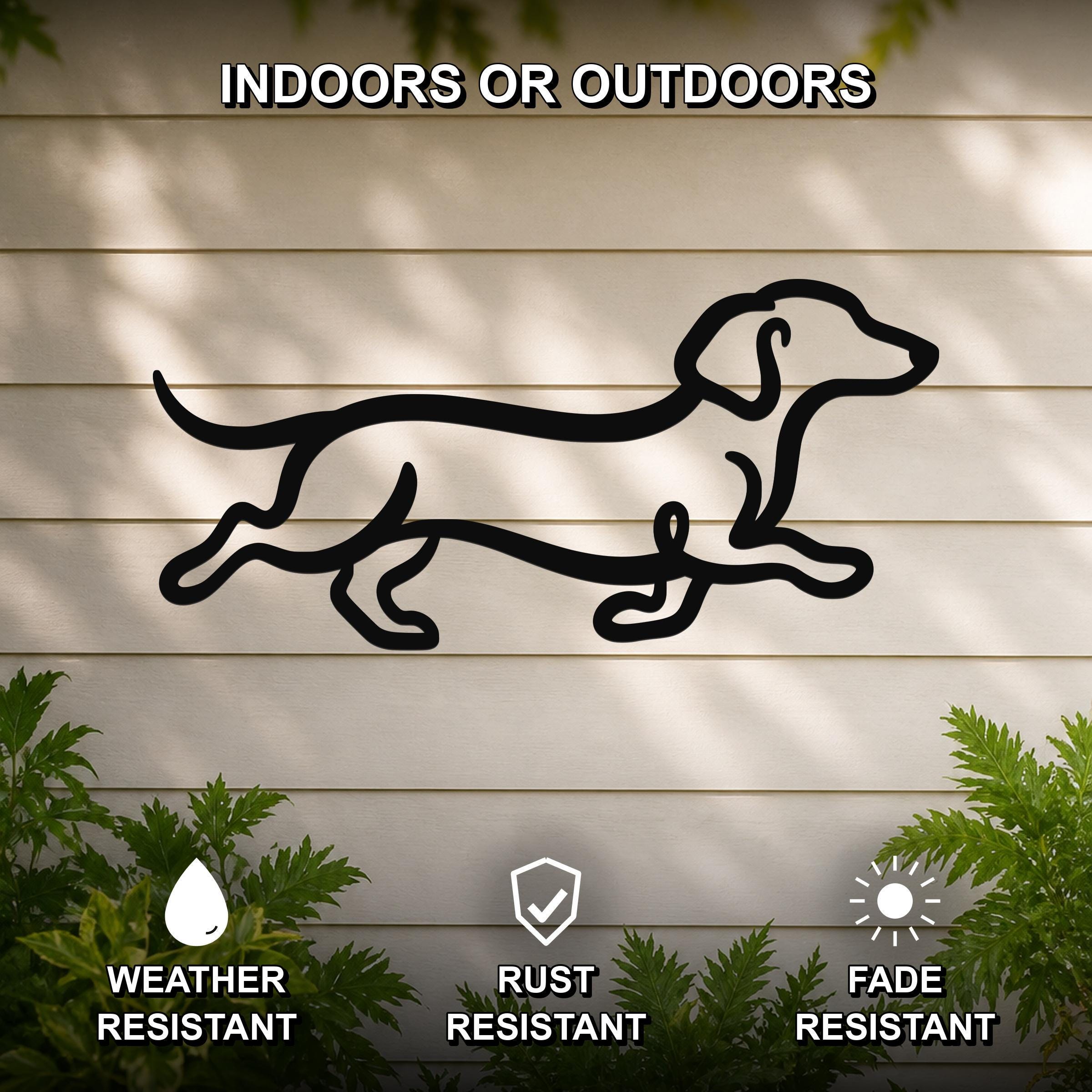 Black metal dachshund wall art with a running silhouette, mounted on a light-colored outdoor wall with greenery below.