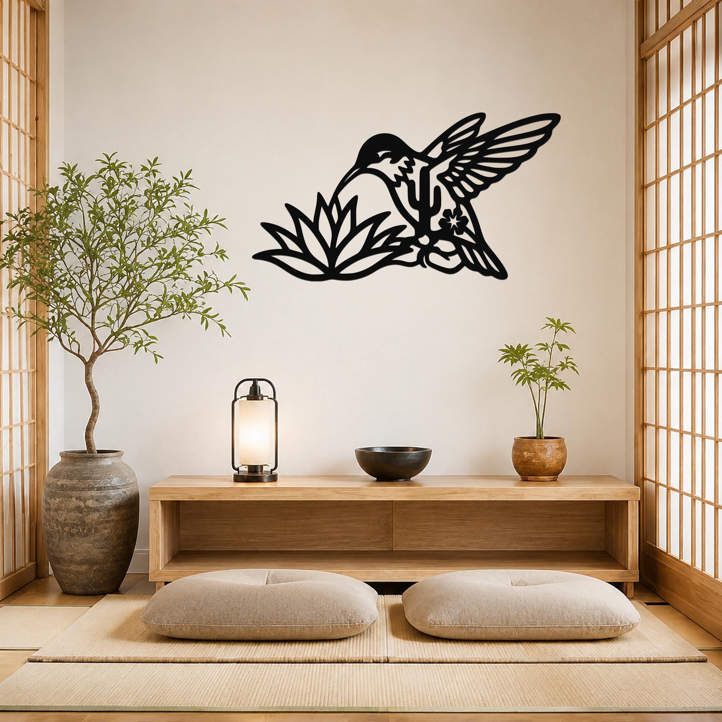 Black metal hummingbird wall art with floral and leaf cutouts, mounted on a wall above a wooden console in a minimalist room.