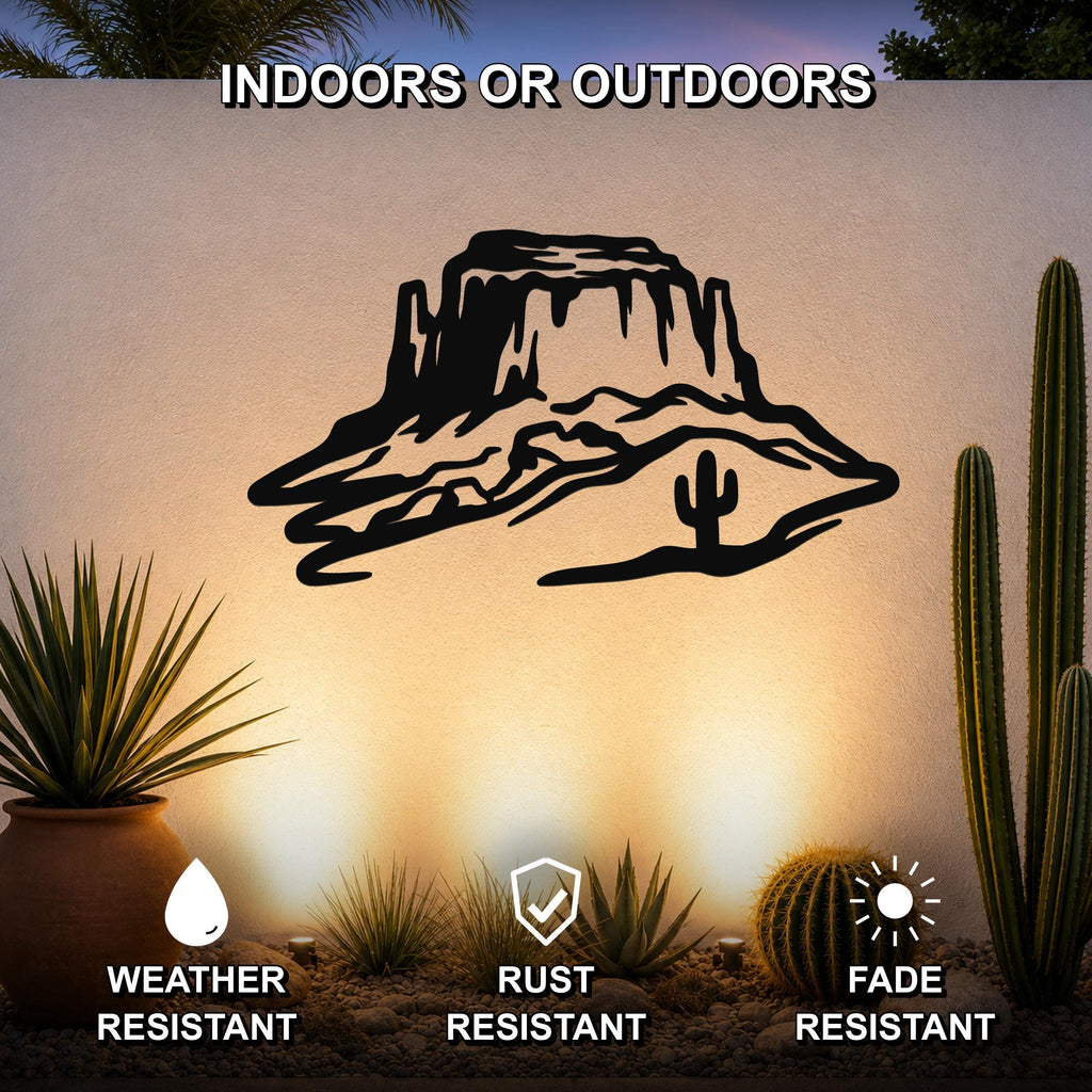 Black metal wall art featuring a desert mesa silhouette with cactus and rock formations, mounted on an outdoor wall above a desert garden with cacti and pebbles.
