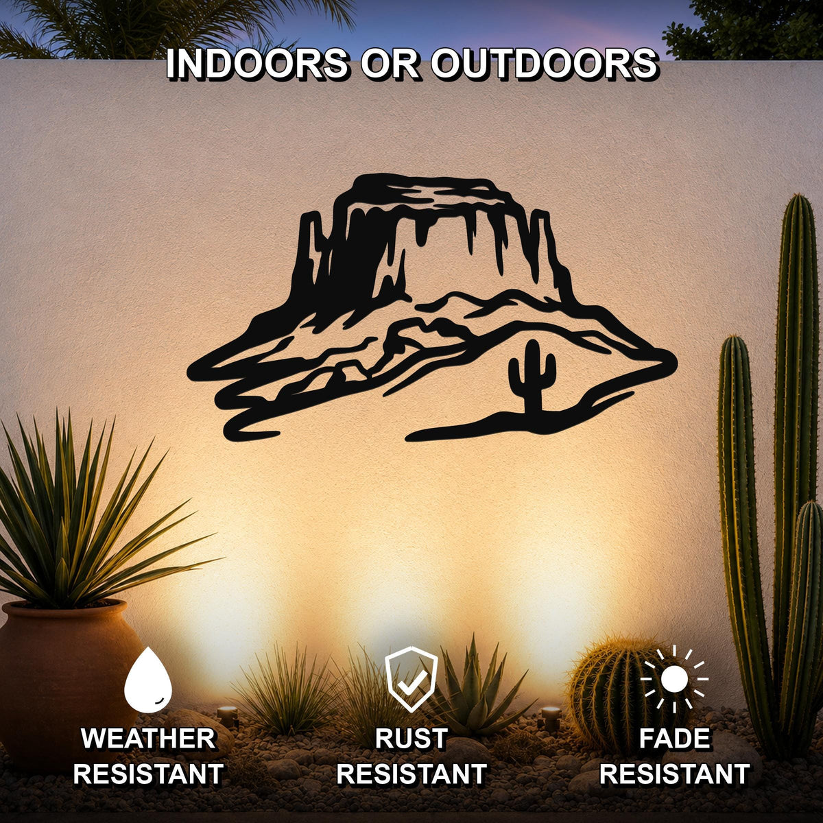 Black metal wall art featuring a desert mesa silhouette with cactus and rock formations, mounted on an outdoor wall above a desert garden with cacti and pebbles.