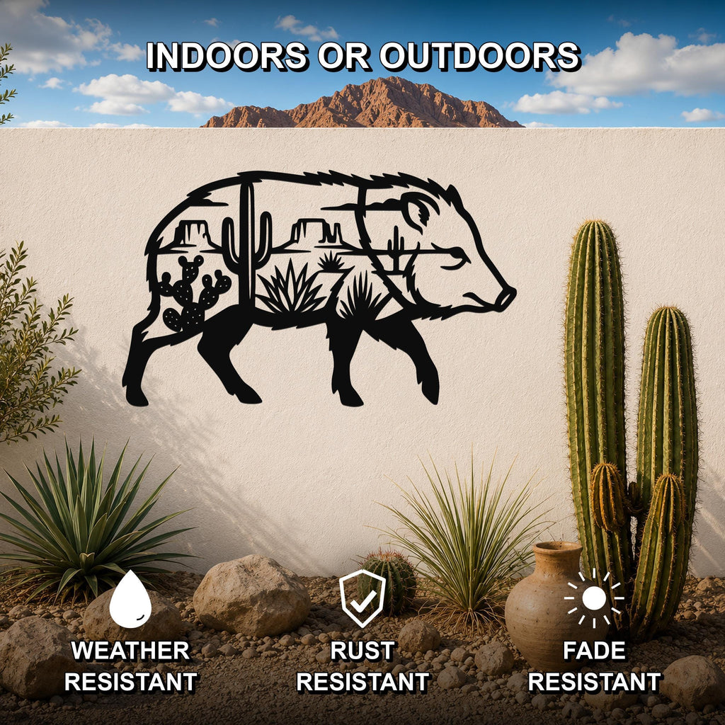 Black metal wall art of a javelina silhouette with desert cactus and mountain cutouts, mounted on an outdoor wall in a desert landscape.