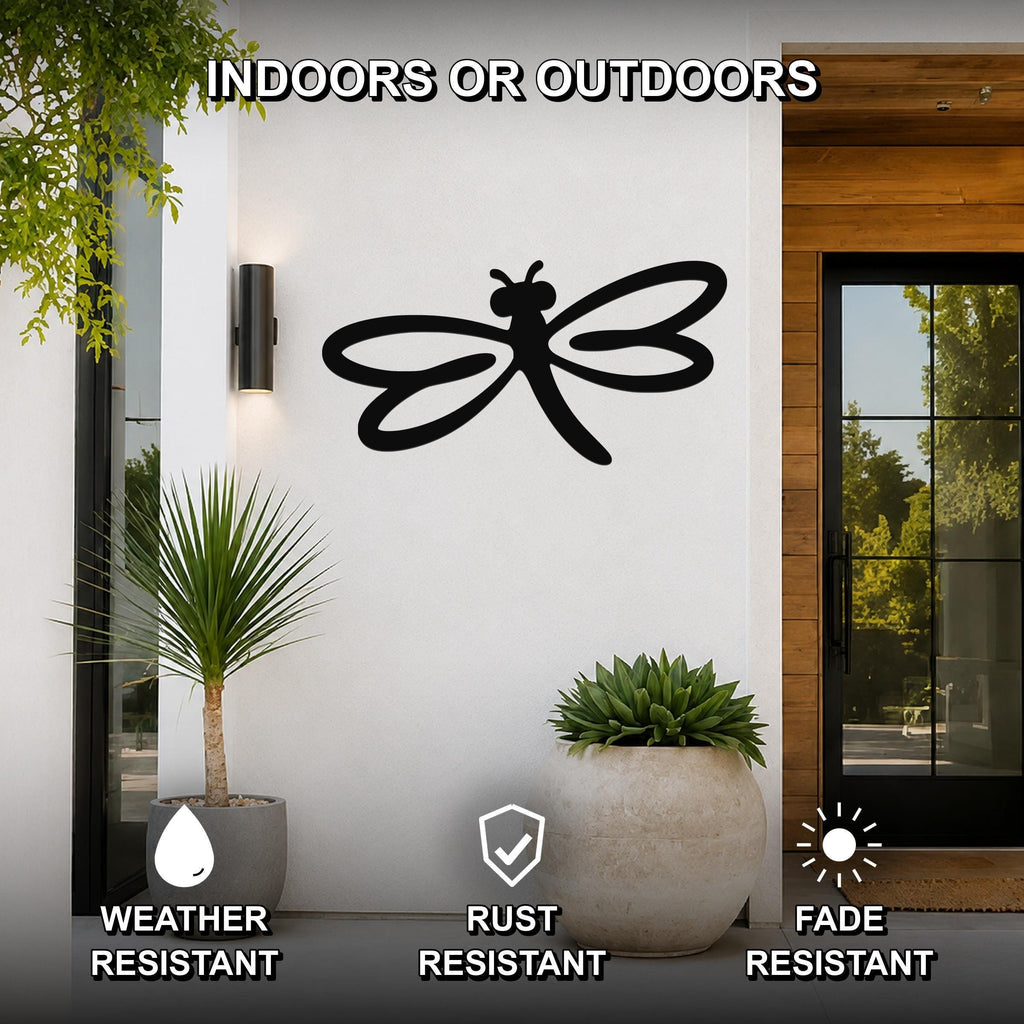 Black metal dragonfly wall art with cutout wings and body, mounted on a white exterior wall beside a glass door and potted plants.