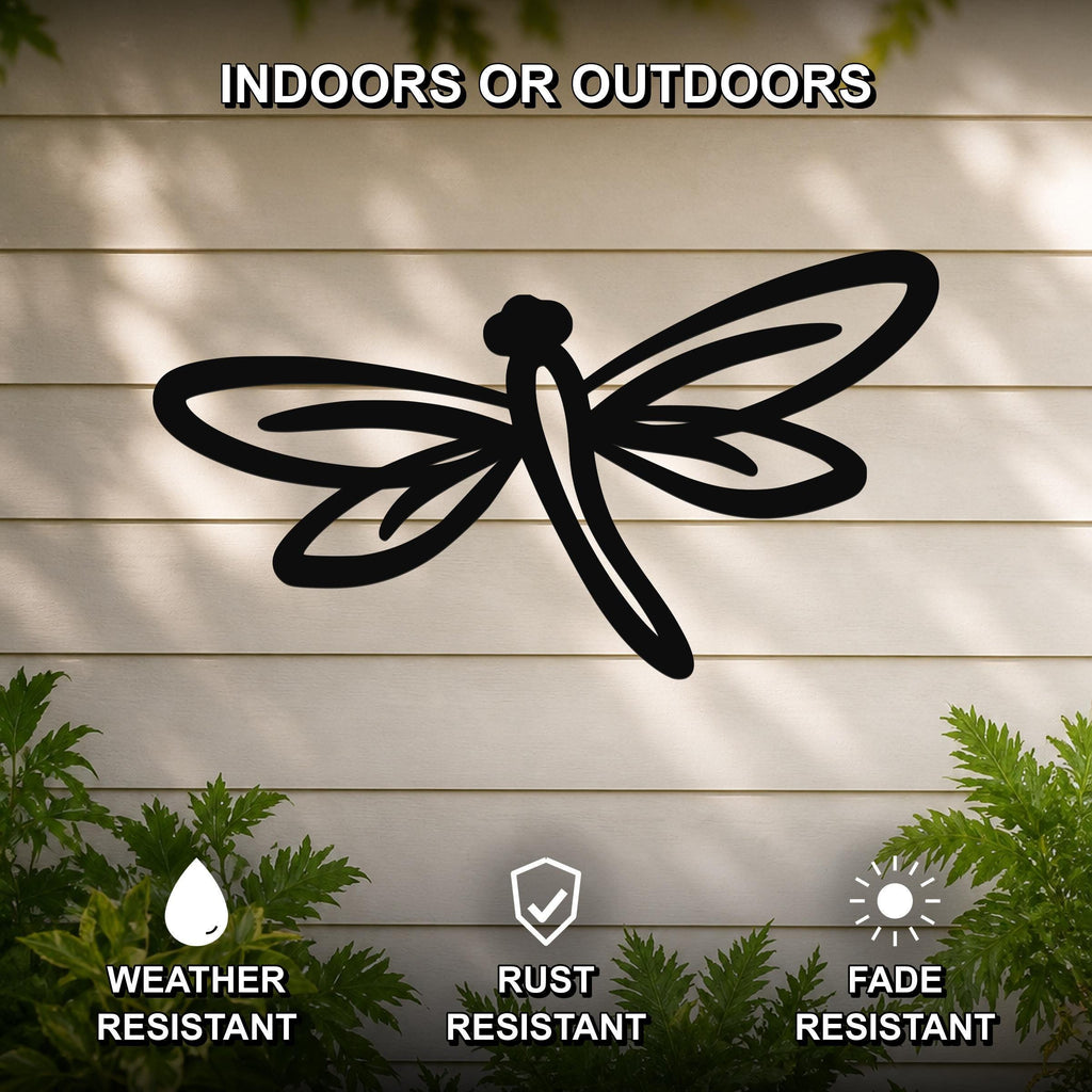 Black metal dragonfly wall art with cutout wings and body, mounted on a light-colored outdoor wall with greenery below.