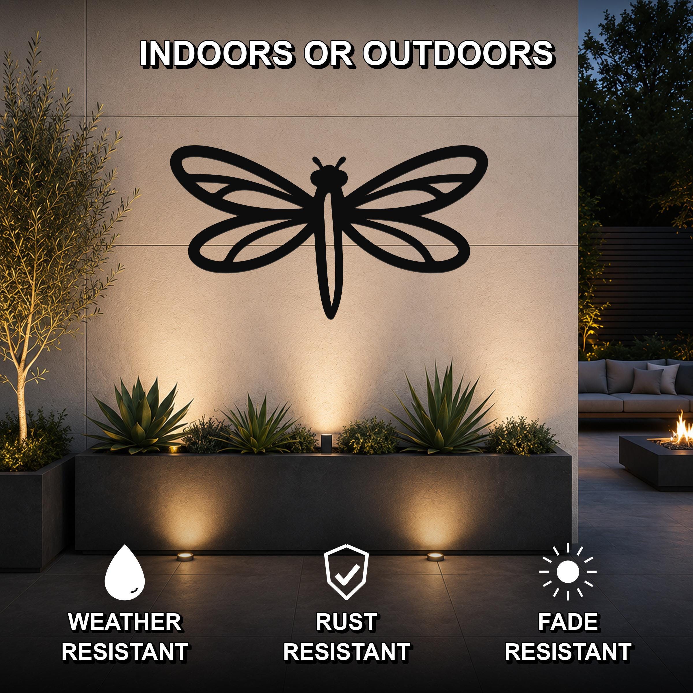 Black metal dragonfly wall art with detailed wing cutouts, mounted on an outdoor wall above a planter in a modern patio setting.