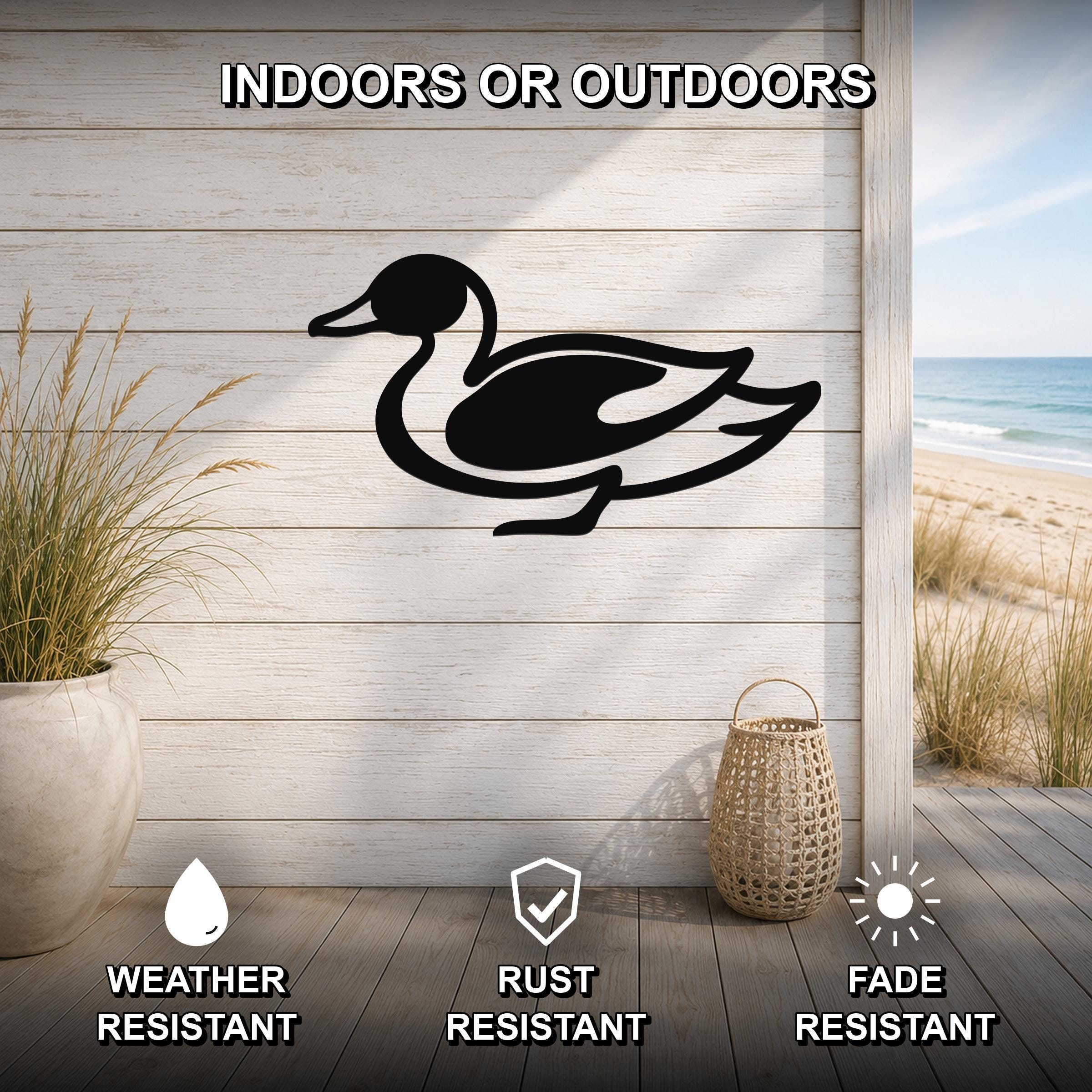 Black metal duck wall sculpture with a silhouette design, mounted on a light wood plank wall in a beach-themed outdoor space with a view of the ocean.