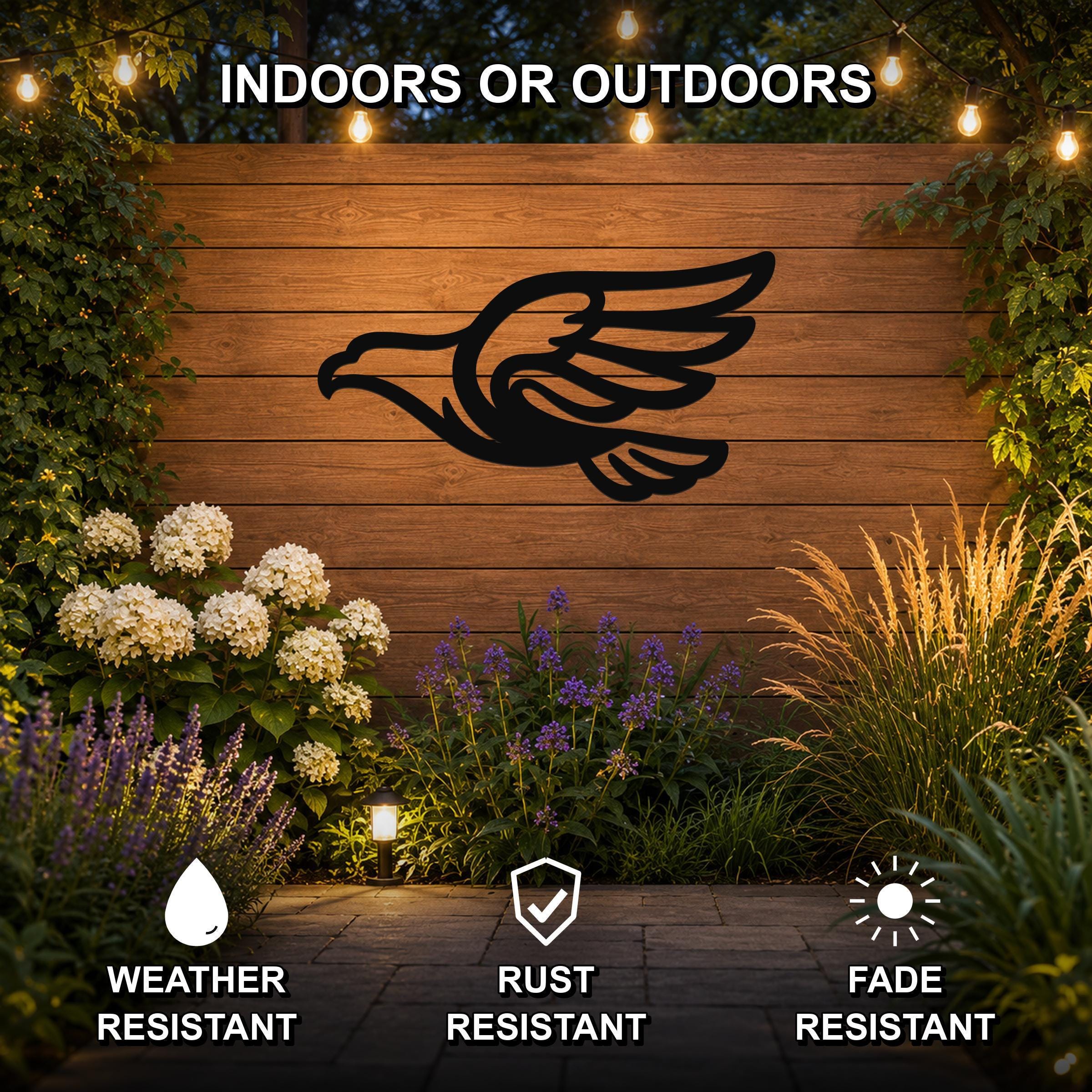 Black metal eagle silhouette wall art mounted on a wooden outdoor wall, displayed above a garden with flowers and string lights, weather, rust, and fade resistant.