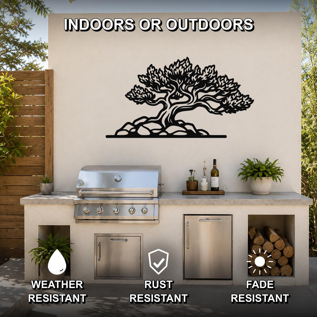 Black metal wall art in the silhouette of a juniper tree with detailed branches and roots, mounted on an outdoor kitchen wall above a stainless steel grill.