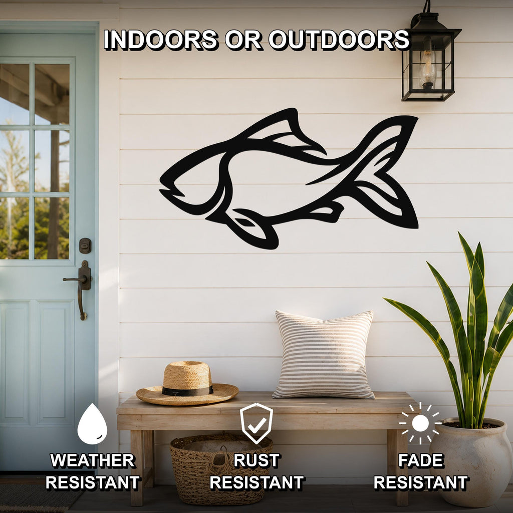 Black metal fish wall art with internal cutout details, mounted on a white shiplap wall above a wooden bench in a porch setting.
