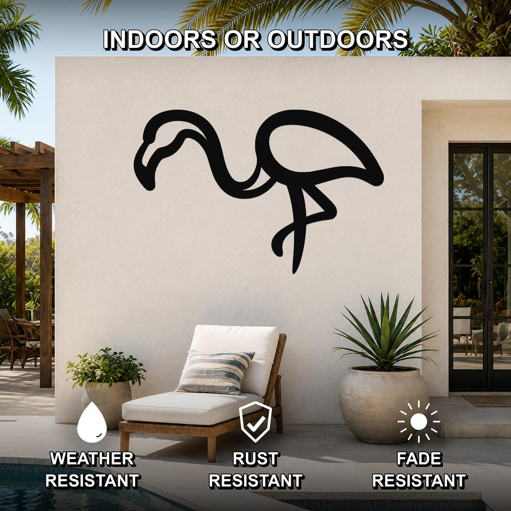Black metal flamingo wall art silhouette mounted on an outdoor patio wall above a lounge chair, with palm trees and a pool visible in the background.