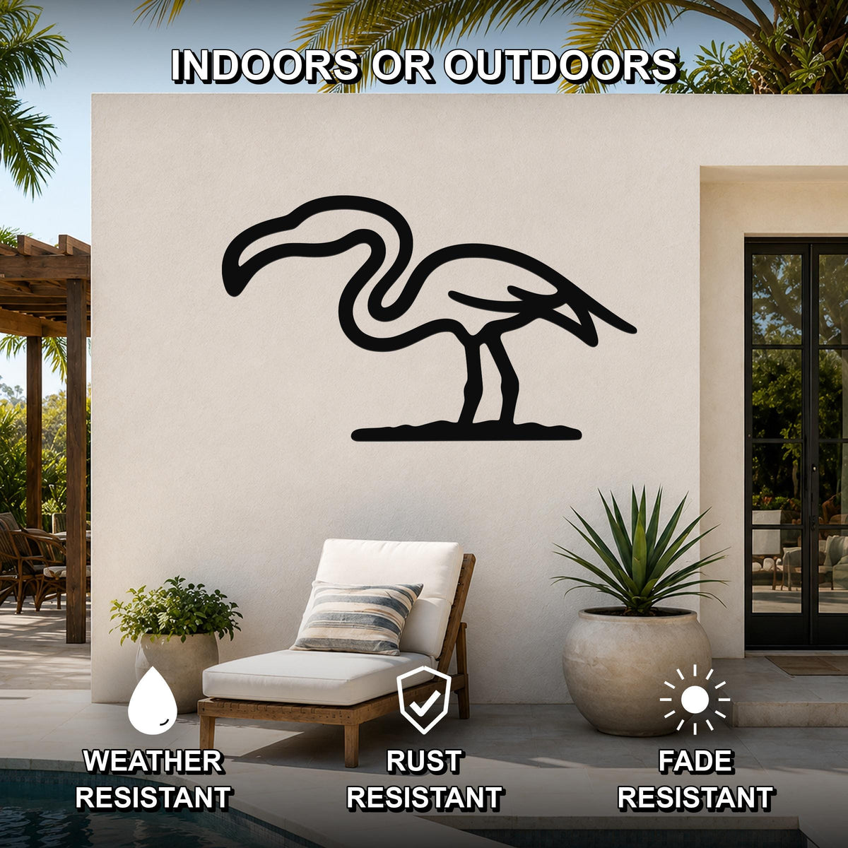 Black metal flamingo wall art silhouette mounted on an outdoor patio wall above a lounge chair, with palm trees and a pool visible in the background.