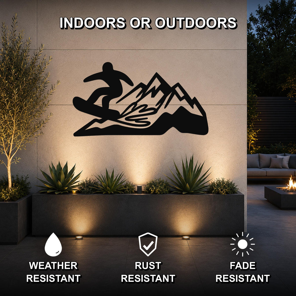 Black metal wall art featuring a snowboarder silhouette over mountain peaks, mounted on an outdoor wall above a planter with accent lighting.