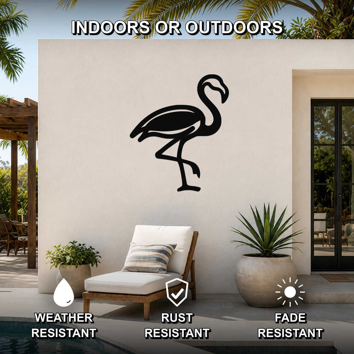 Black metal flamingo wall art silhouette mounted on an outdoor patio wall above a lounge chair, with palm trees and a pool visible in the background.
