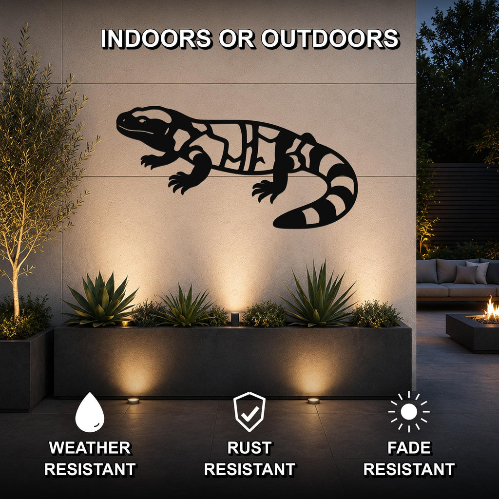 Black metal Gila monster wall art with internal cutout patterns, mounted on an outdoor wall above a planter in a modern patio setting.