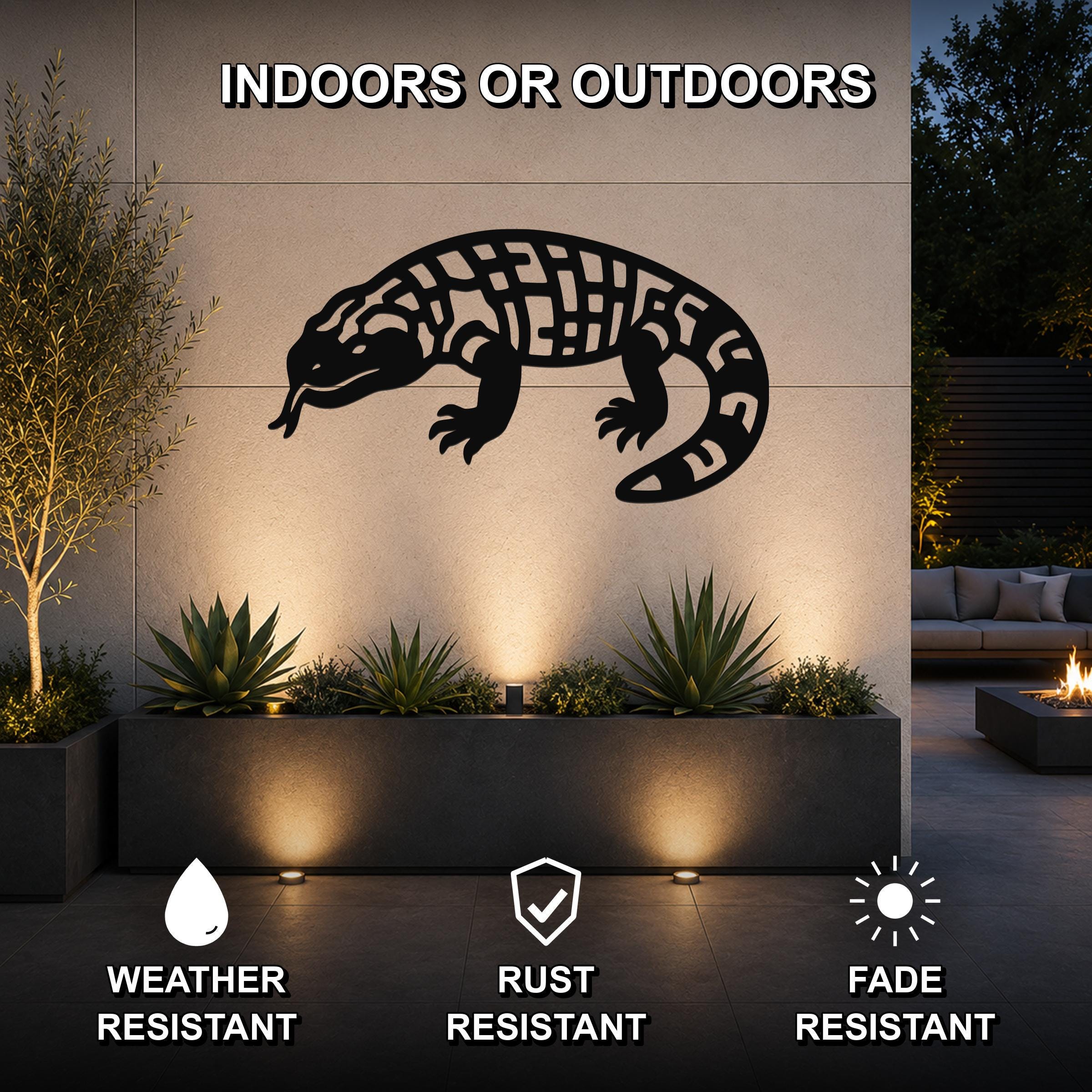 Black metal Gila monster wall art with intricate internal cutouts, mounted on an outdoor wall above a planter in a modern patio setting.