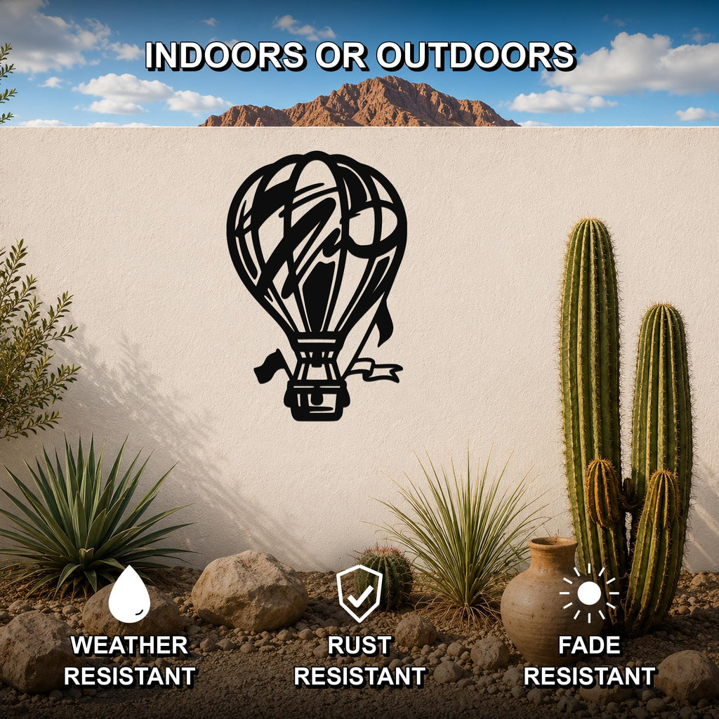Black metal hot air balloon wall art with internal cutout details, mounted on an outdoor wall in a desert garden setting.