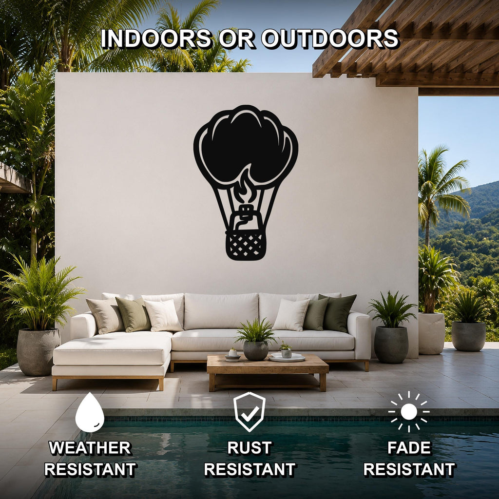 Black metal hot air balloon wall art with flame and basket cutouts, mounted on a white outdoor wall above a sofa in a patio living area.