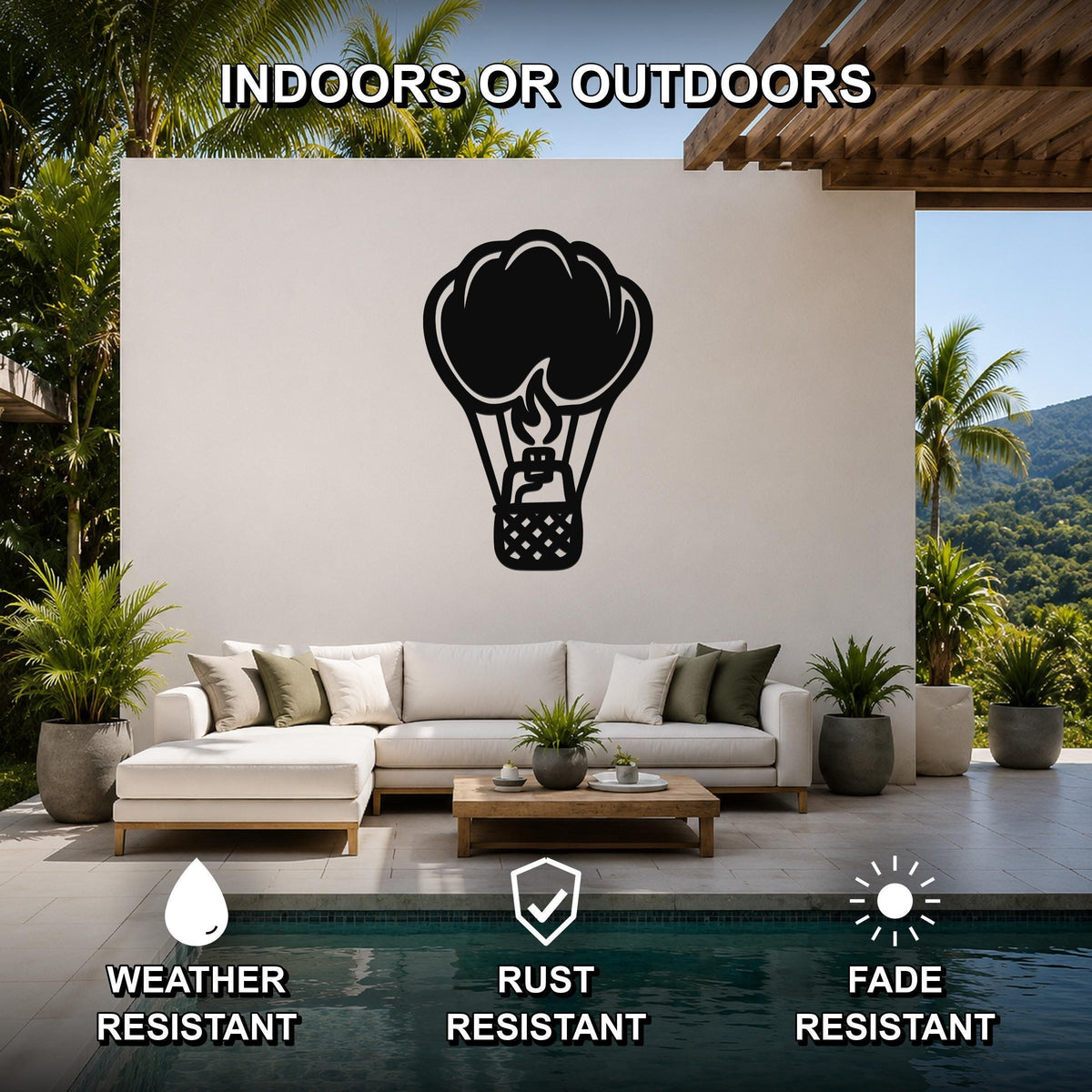 Black metal hot air balloon wall art with flame and basket cutouts, mounted on a white outdoor wall above a sofa in a patio living area.