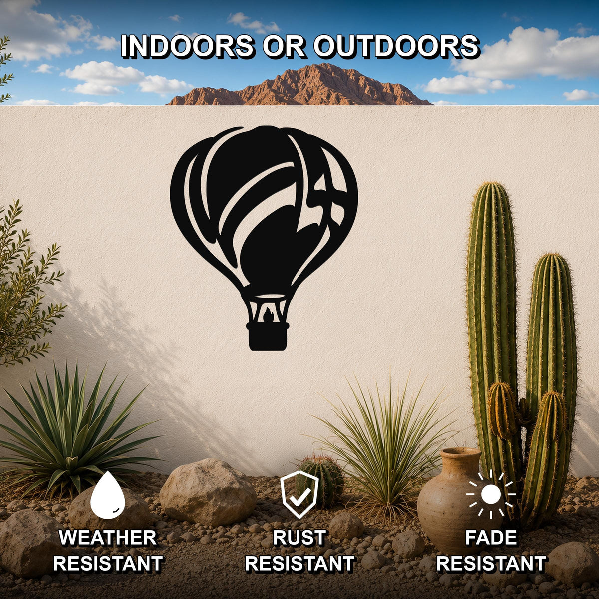 Black metal hot air balloon wall art with internal flame and basket cutouts, mounted on an outdoor wall in a desert garden setting.