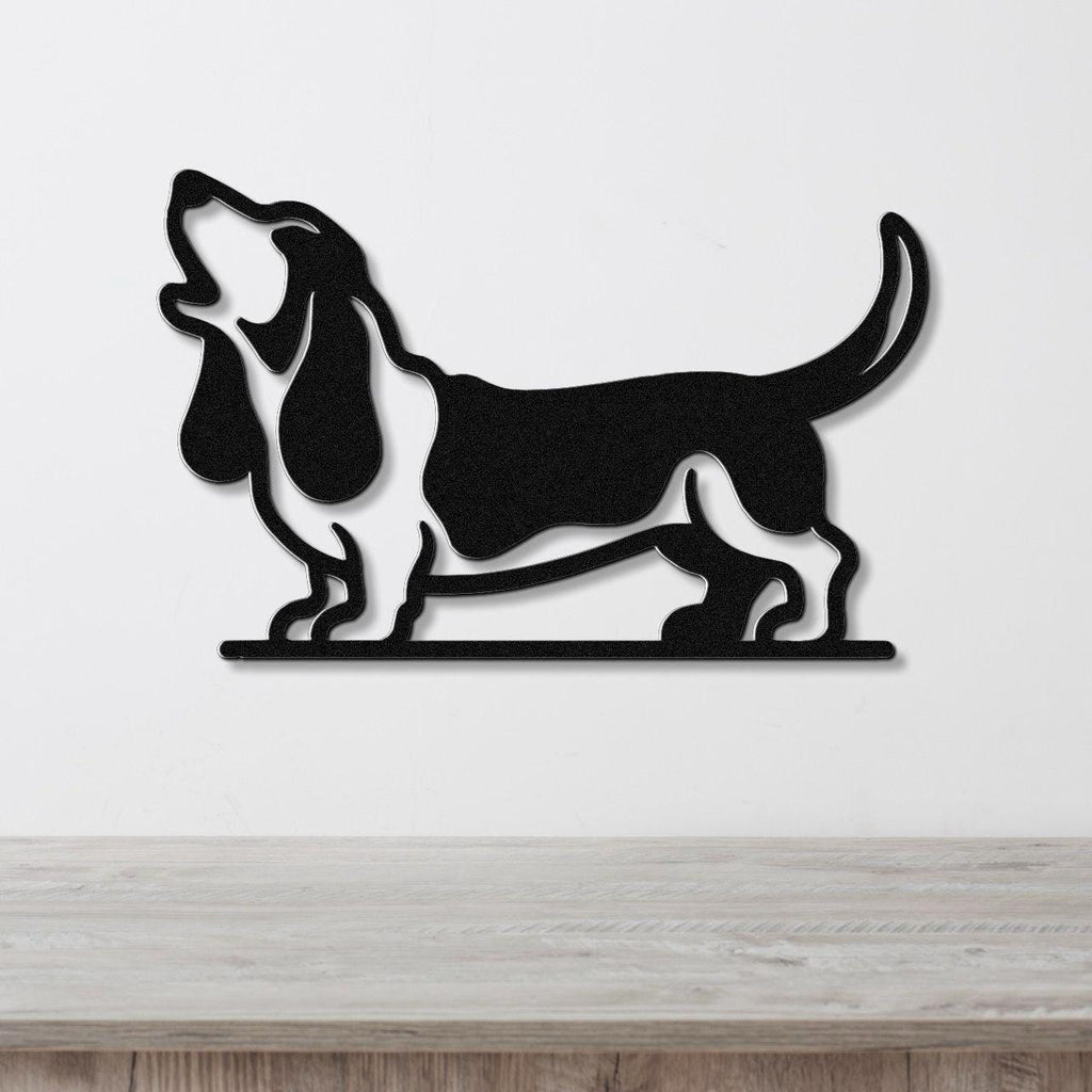 Black metal wall art silhouette of a basset hound howling, mounted on a white wall above a light wood surface.