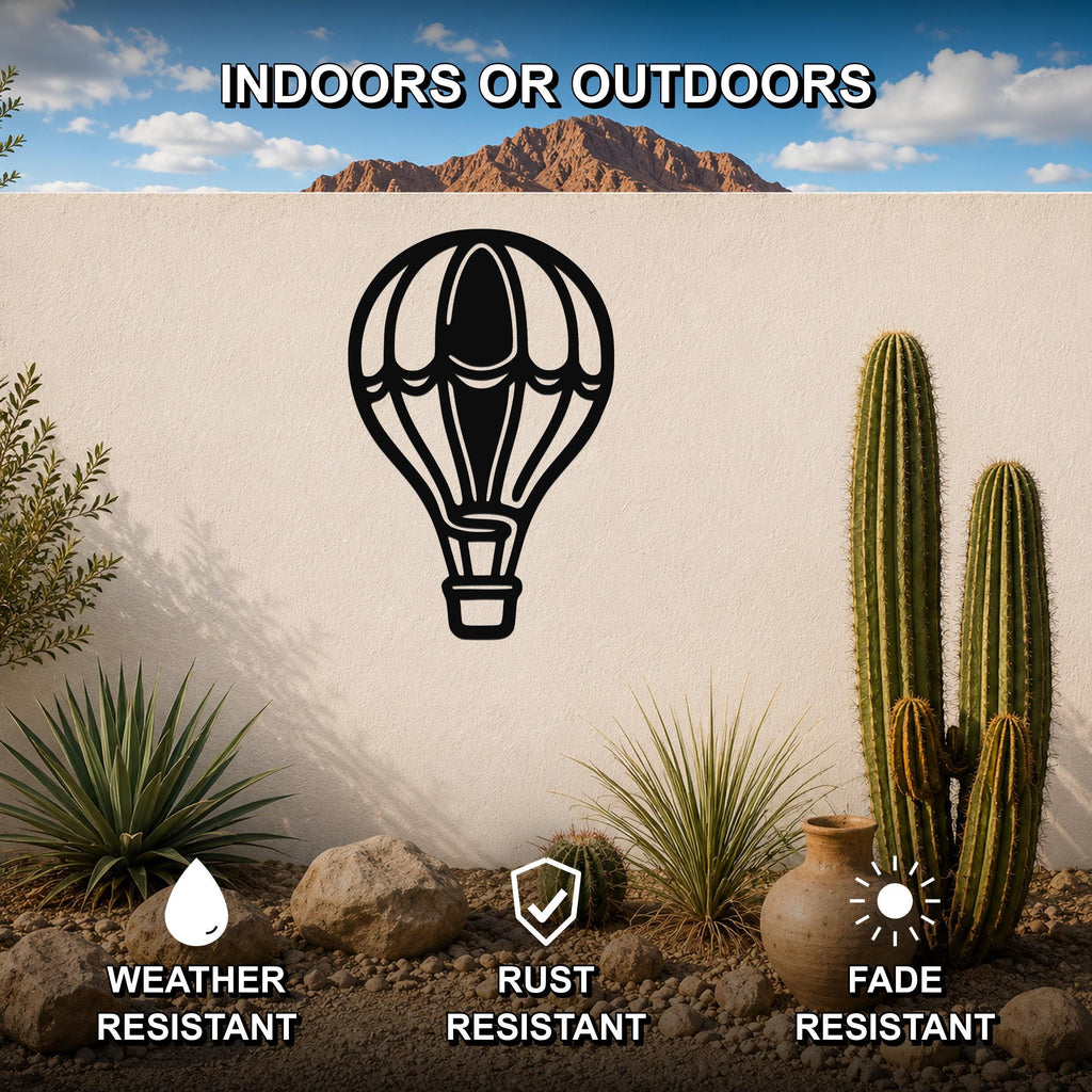 Black metal hot air balloon wall art with internal cutout details, mounted on an outdoor wall in a desert garden setting with cacti and rocks.