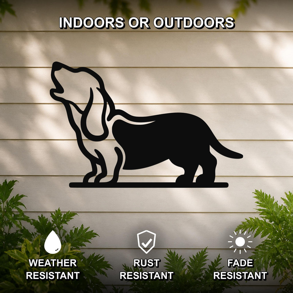 Black metal wall art silhouette of a howling basset hound, mounted on a light-colored outdoor wall with greenery below.