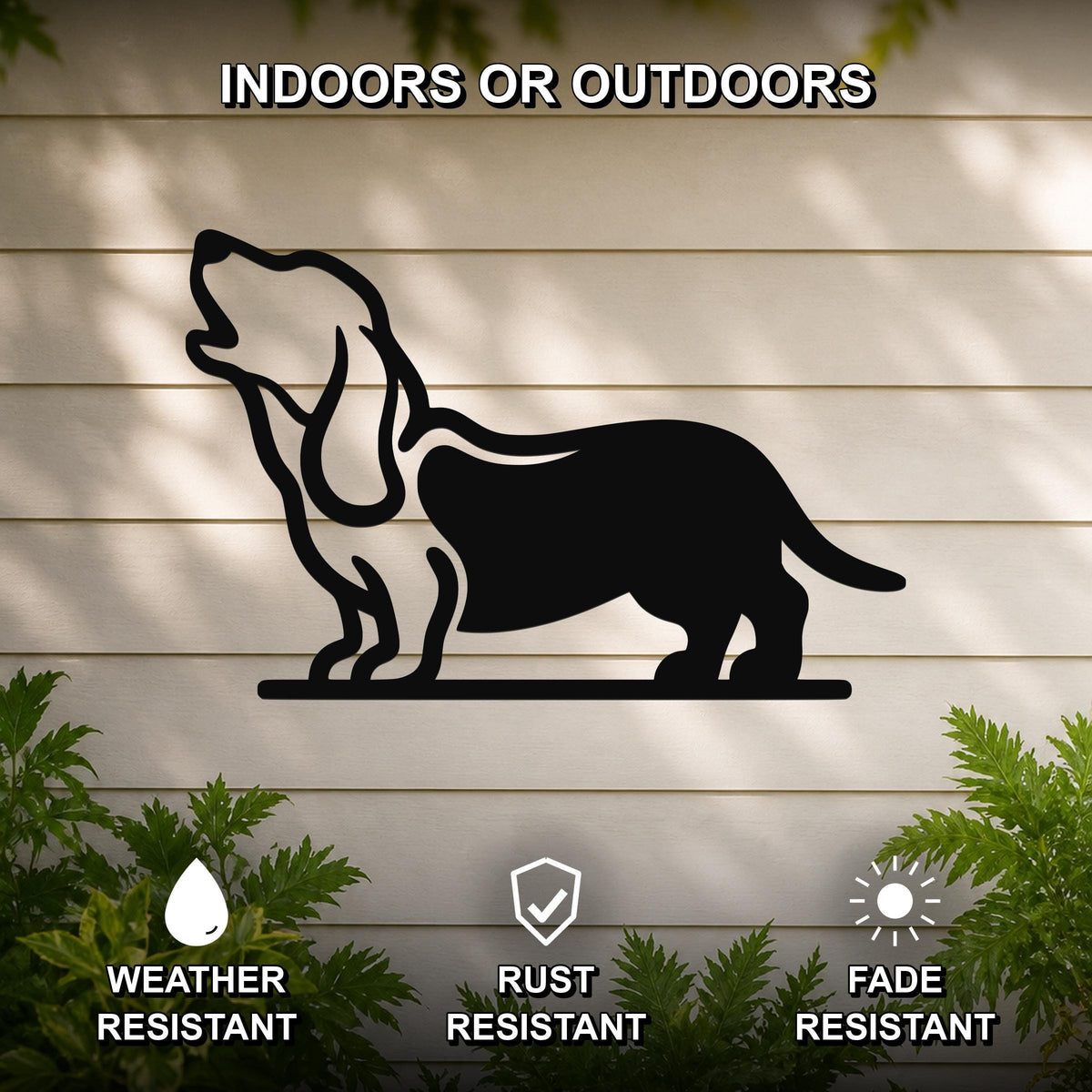 Black metal wall art silhouette of a howling basset hound, mounted on a light-colored outdoor wall with greenery below.