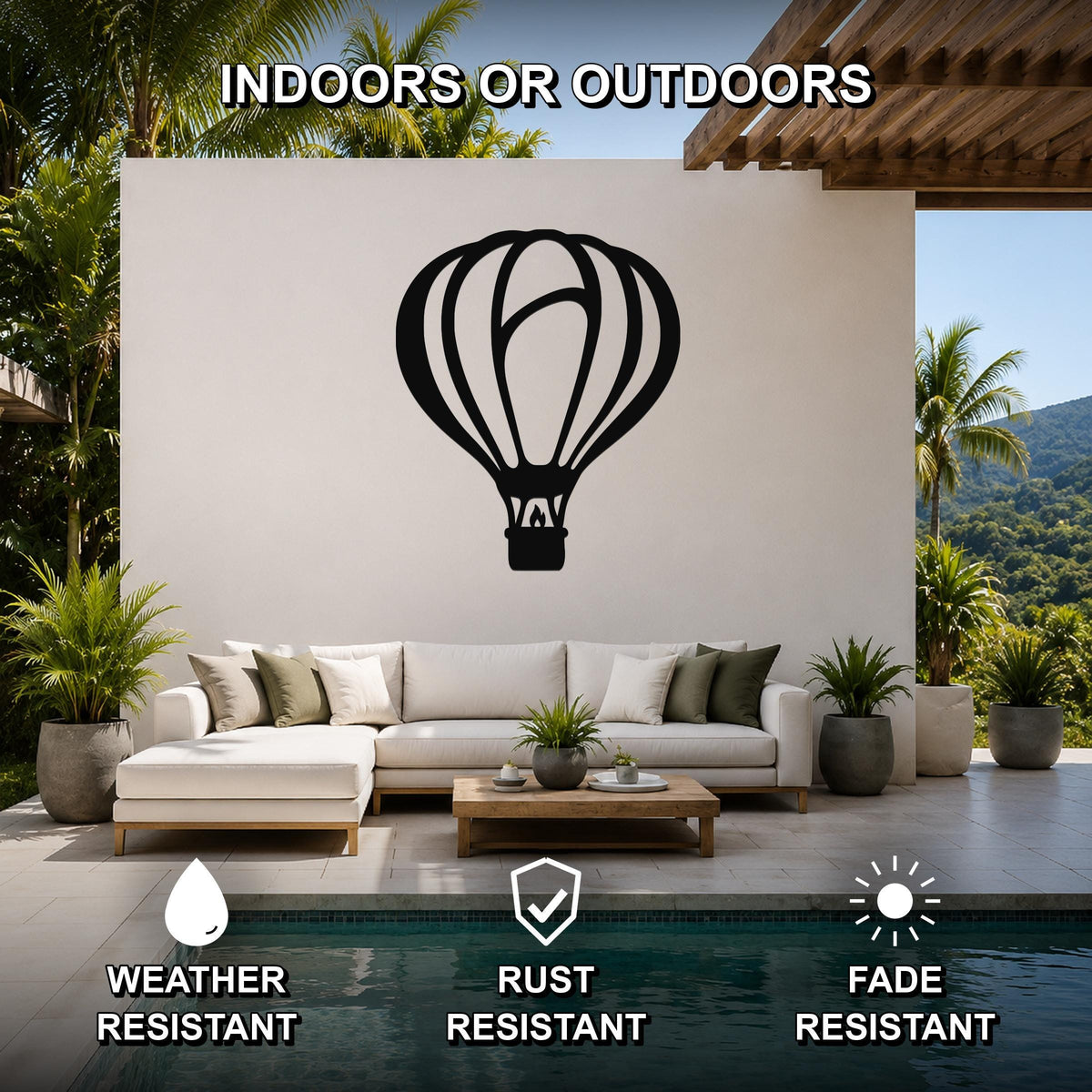 Black metal hot air balloon wall art with internal cutout details, mounted on a white outdoor wall above a sofa in a patio living area.