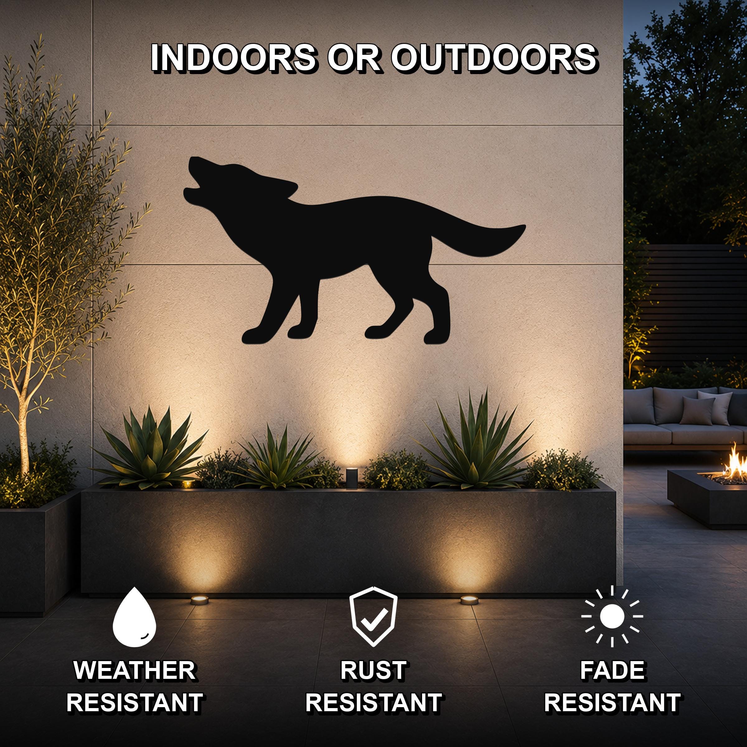Black metal coyote silhouette wall art mounted on an outdoor wall above a planter, shown in a patio setting with uplighting.