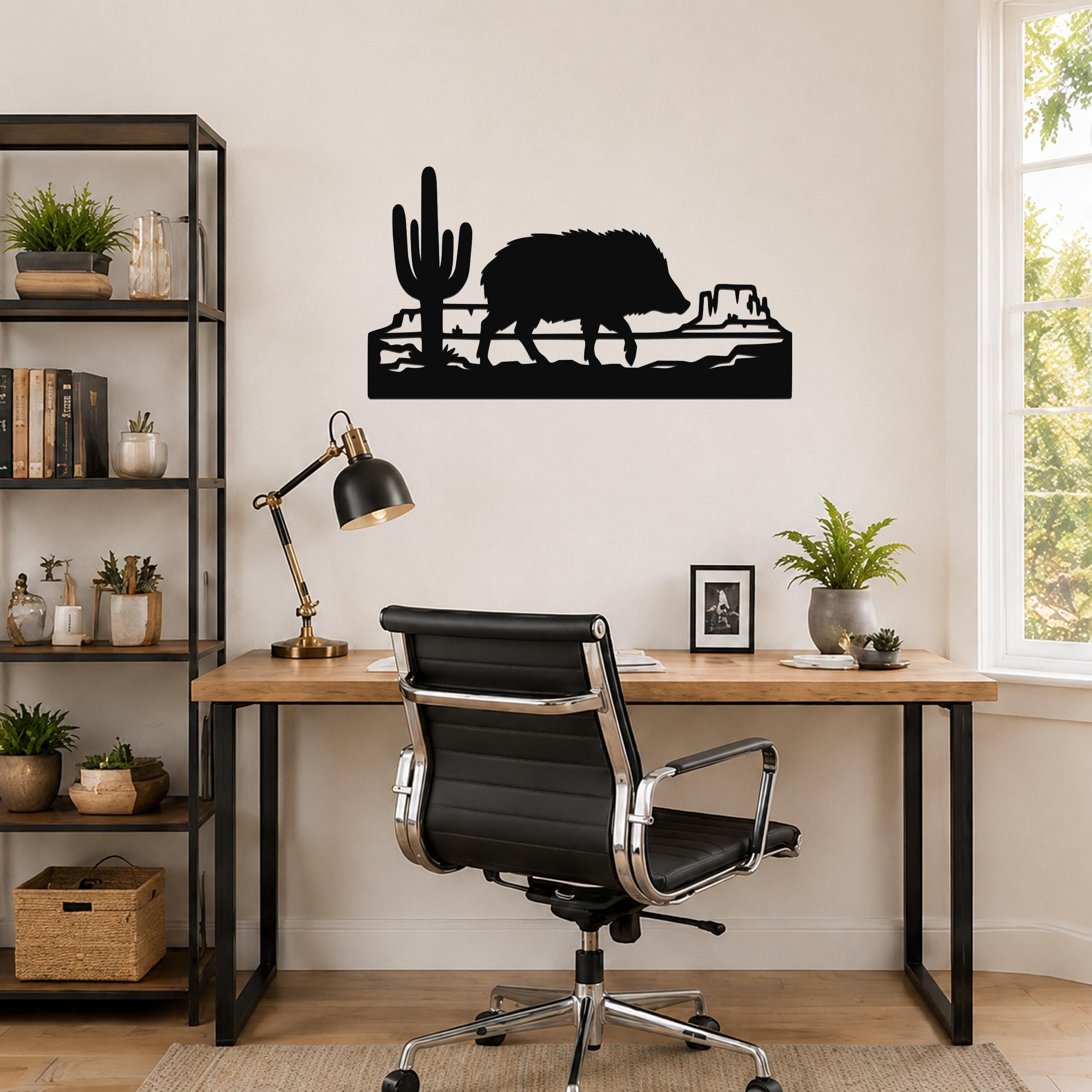 Black metal wall art silhouette of a javelina walking past a saguaro cactus and canyon rock formation, mounted above a wooden desk in a home office.