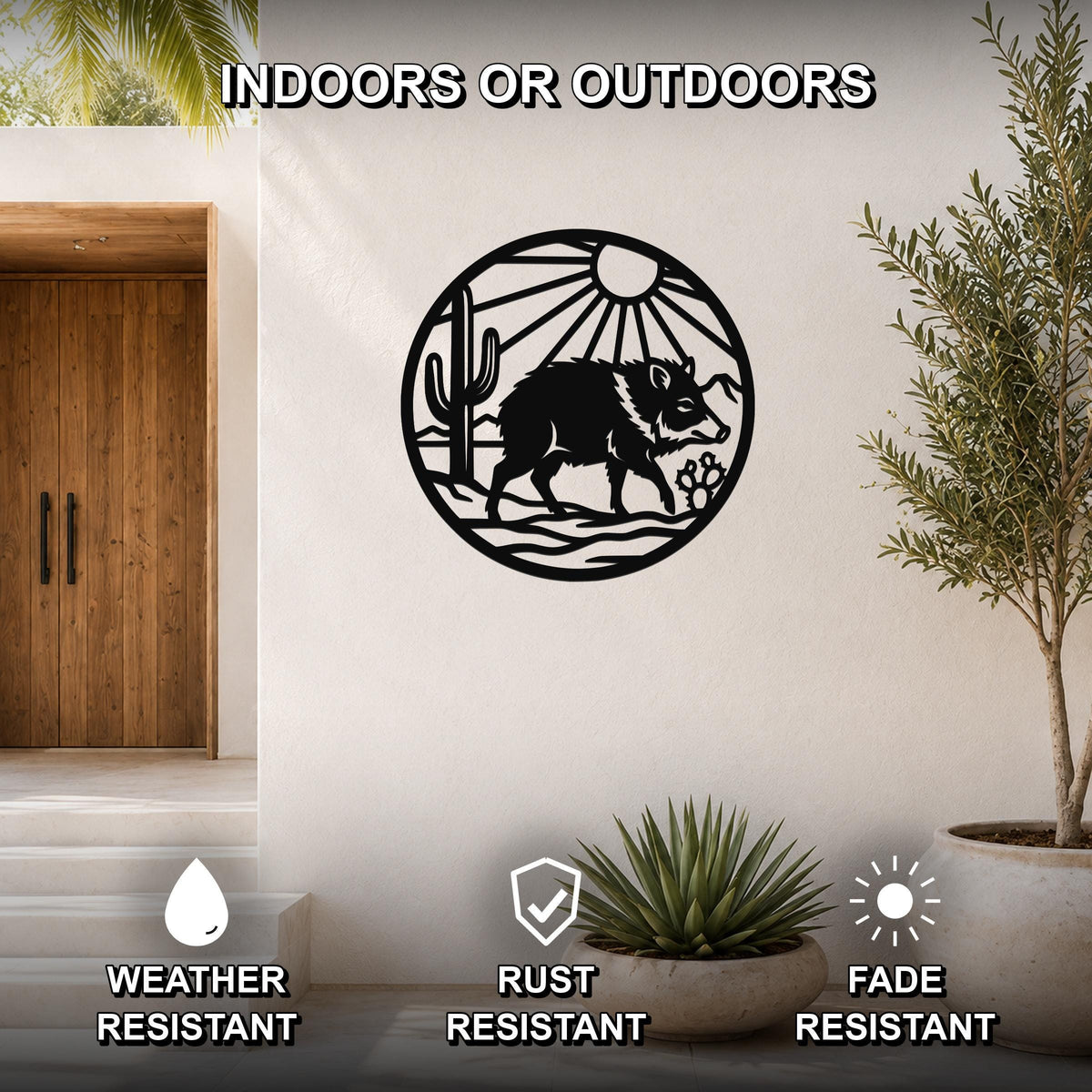 Black metal circular wall art featuring a javelina silhouette with cactus and sun rays, mounted on a white wall in a modern entryway with potted plants.