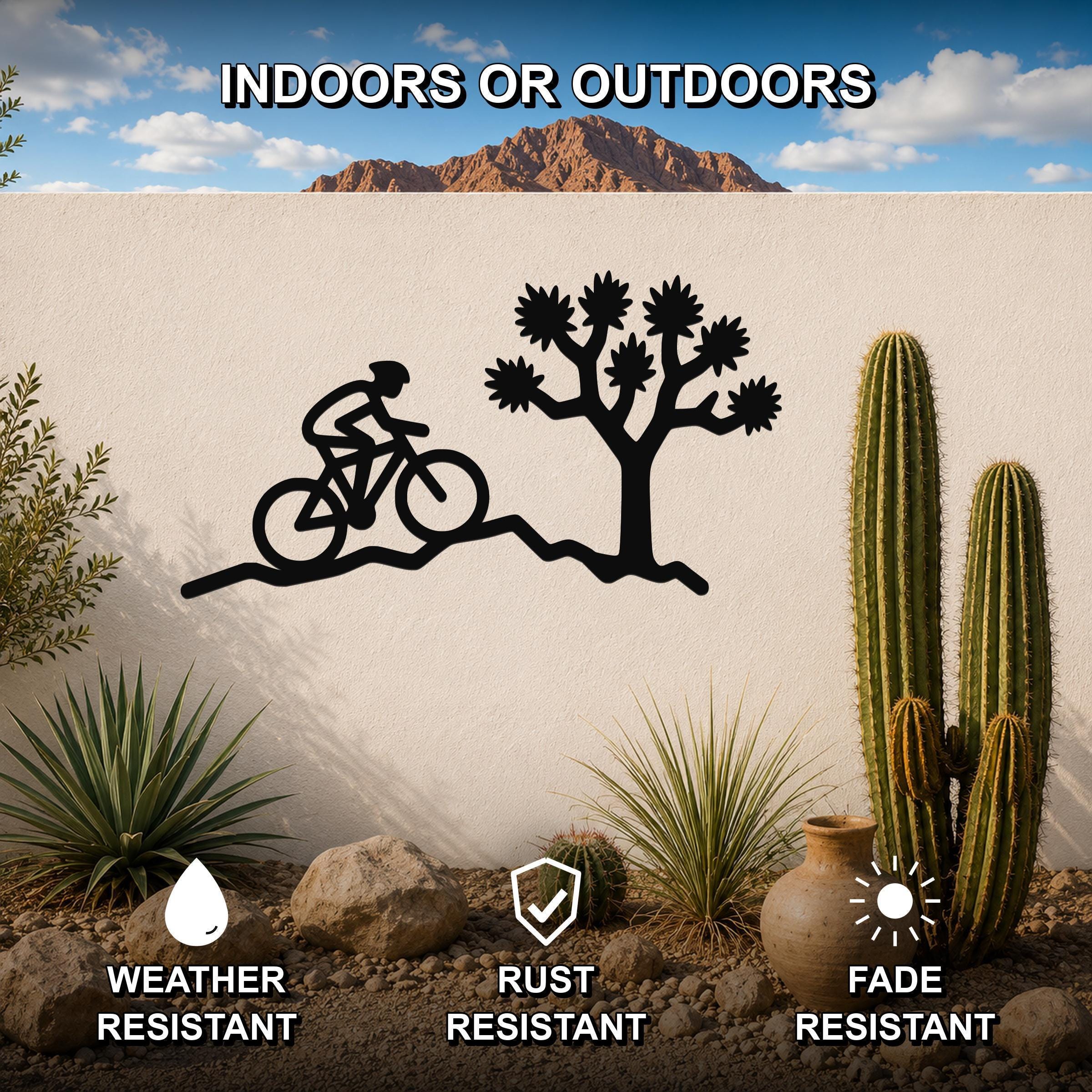 Black metal wall art featuring a cyclist silhouette and a Joshua tree cutout, mounted on an outdoor wall in a desert garden setting.