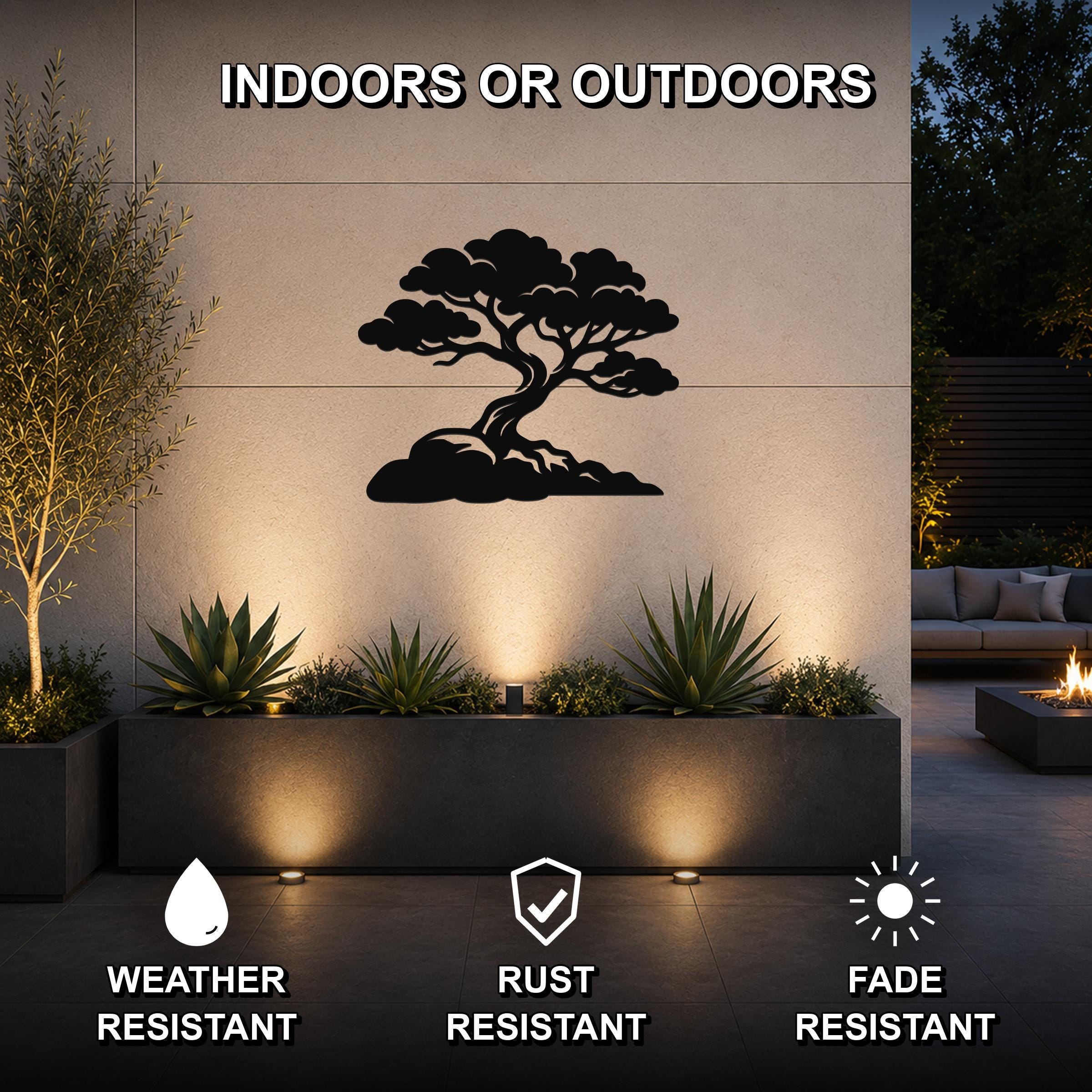 Black metal juniper tree wall art with a silhouette design, mounted on an outdoor wall above a planter in a modern patio setting.