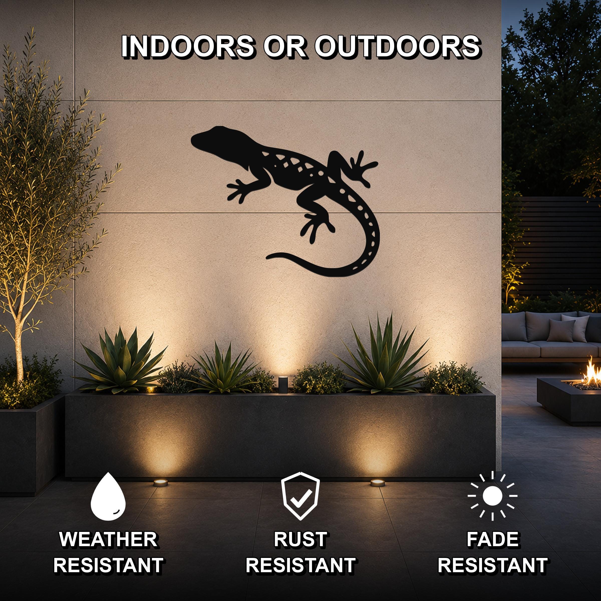 Black metal lizard wall art with internal cutout details, mounted on an outdoor wall above a planter in a patio setting.