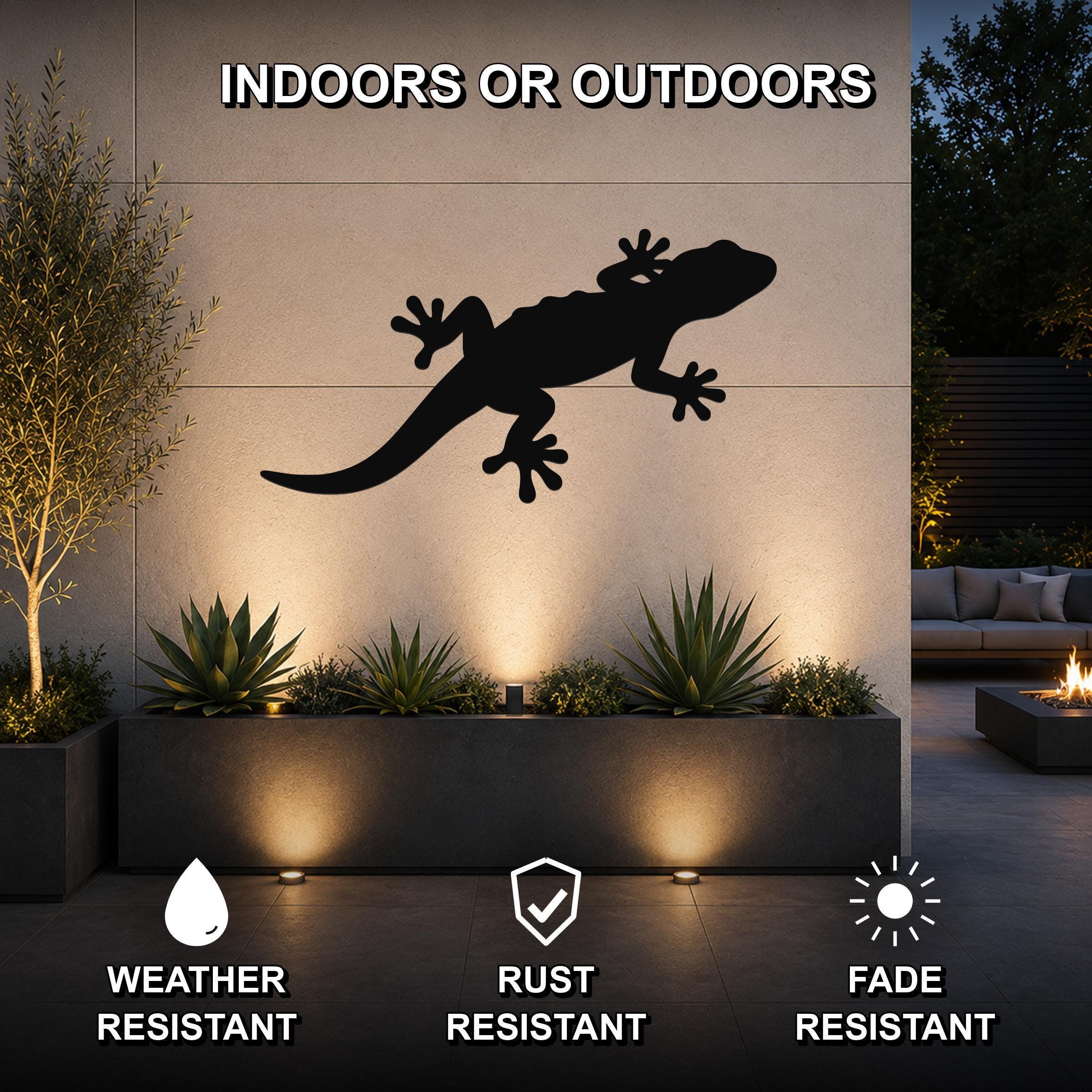 Black metal lizard wall art silhouette mounted on an outdoor wall above a planter, with text indicating it is weather, rust, and fade resistant for indoor or outdoor use.