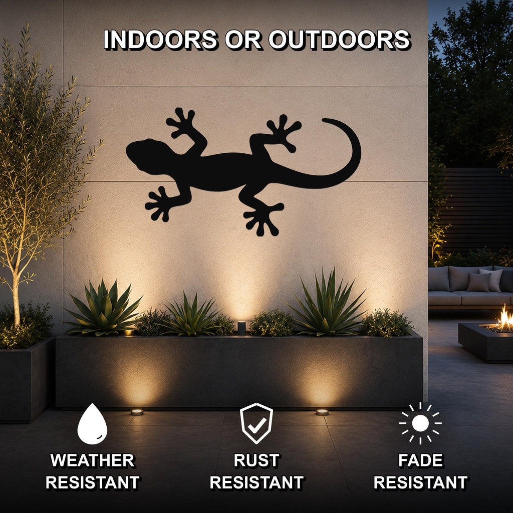 Black metal lizard wall art silhouette mounted on an outdoor wall above a planter, illuminated by uplights in a modern patio setting.