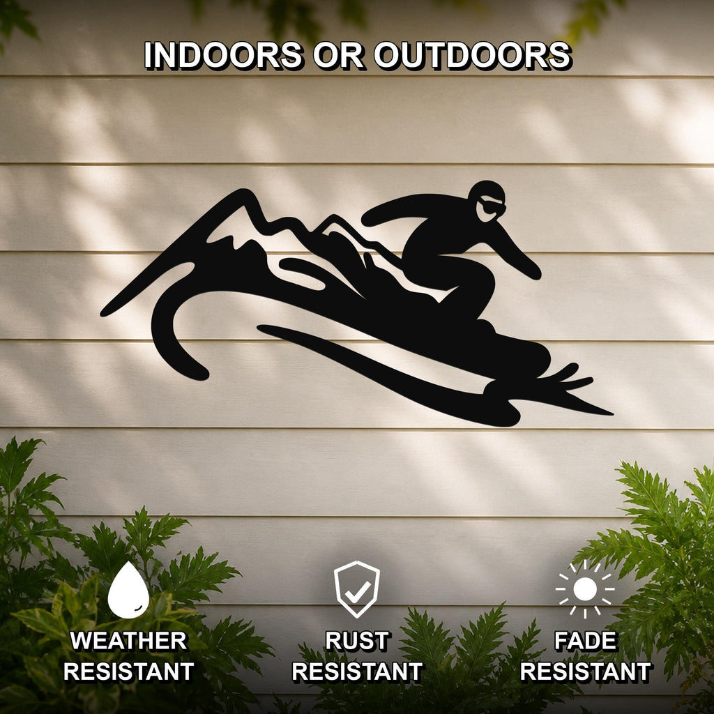 Black metal wall art silhouette of a snowboarder in motion over mountain peaks, mounted on a light-colored outdoor wall with greenery below.