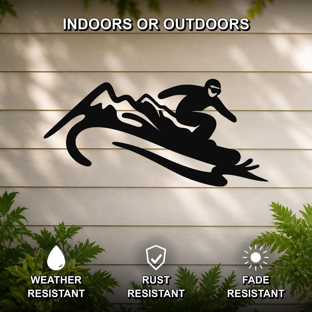 Black metal wall art silhouette of a snowboarder in motion over mountain peaks, mounted on a light-colored outdoor wall with greenery below.