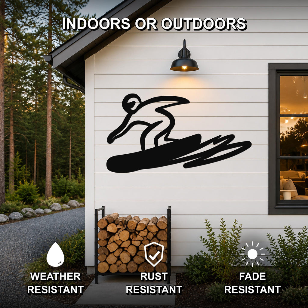 Black metal wall art featuring a bold silhouette of a snowboarder in motion, mounted on a white exterior wall above a firewood rack, with text indicating it is weather, rust, and fade resistant for indoor or outdoor use.