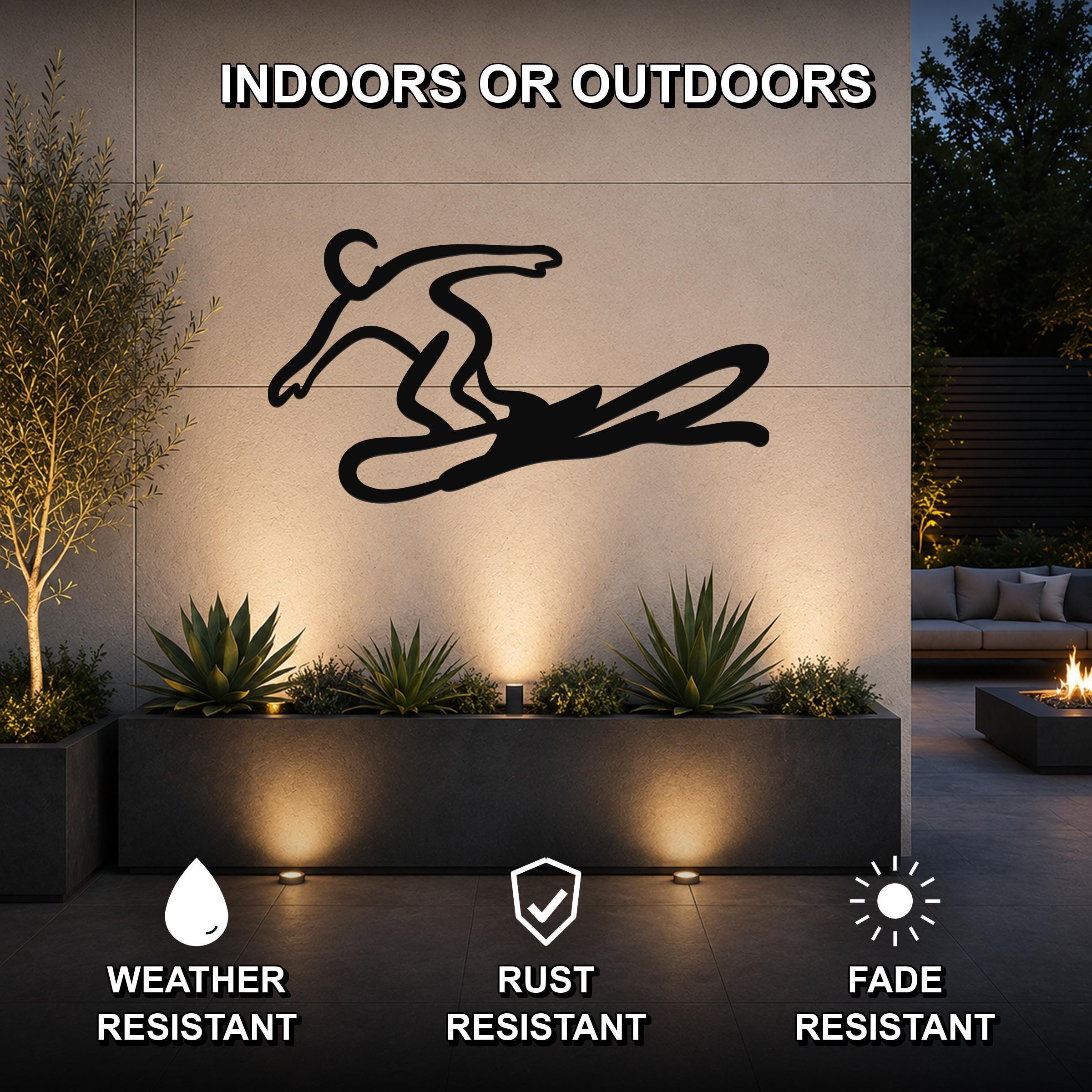 Black metal wall art of a snowboarder silhouette with motion-line cutouts, mounted on an outdoor wall above a planter in a modern patio setting.
