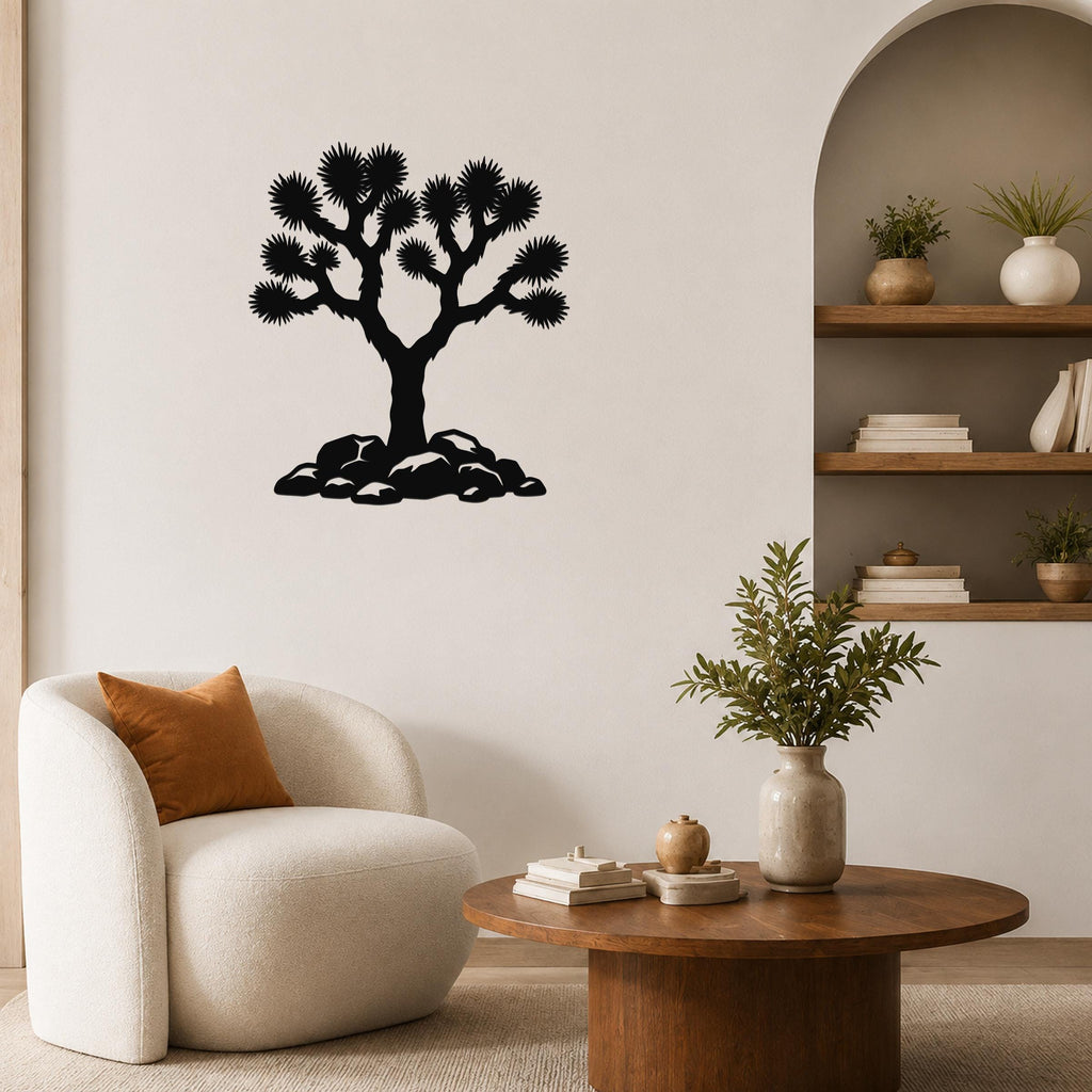 Black metal wall art silhouette of a Joshua tree with spiky branches and rocks at its base, mounted on a living room wall above a white armchair.