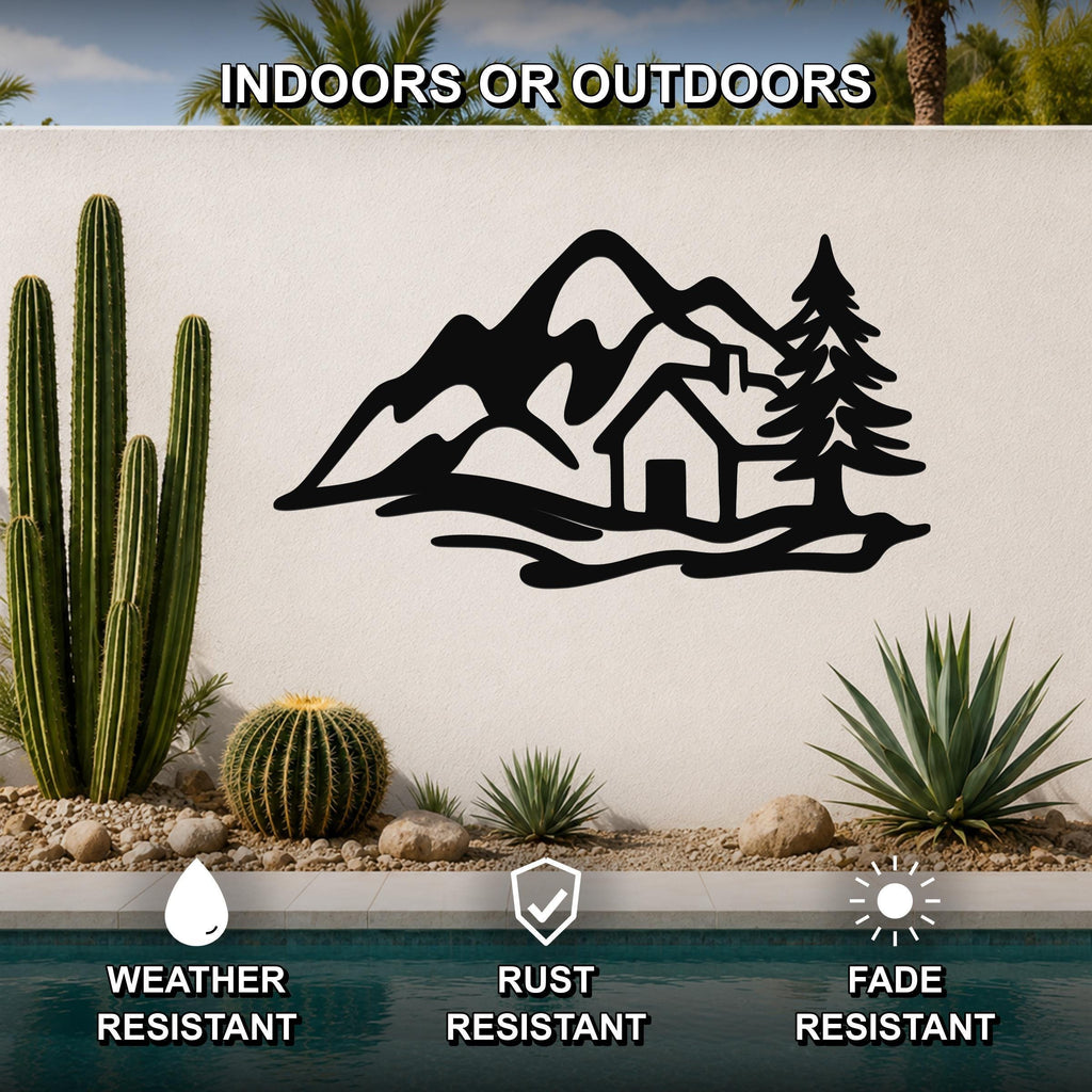 Black metal wall art silhouette of a mountain cabin scene with trees and peaks, mounted on an outdoor wall above a pool with cacti and desert plants.