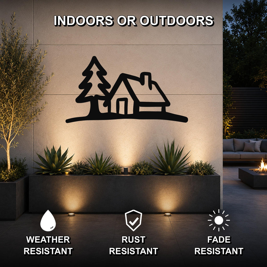 Black metal wall art silhouette of a cabin and tree, mounted on an outdoor wall above a planter with warm lighting, weather resistant, rust resistant, fade resistant.