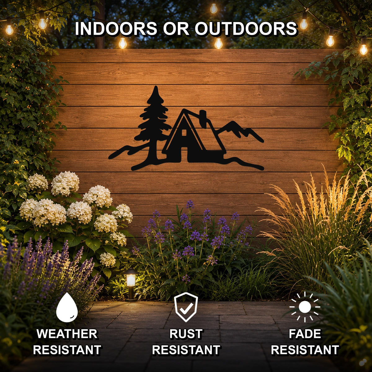Black metal wall art featuring a minimalist silhouette of a cabin, tree, and mountains, mounted on a wooden outdoor wall with string lights and plants, weather, rust, and fade resistant.