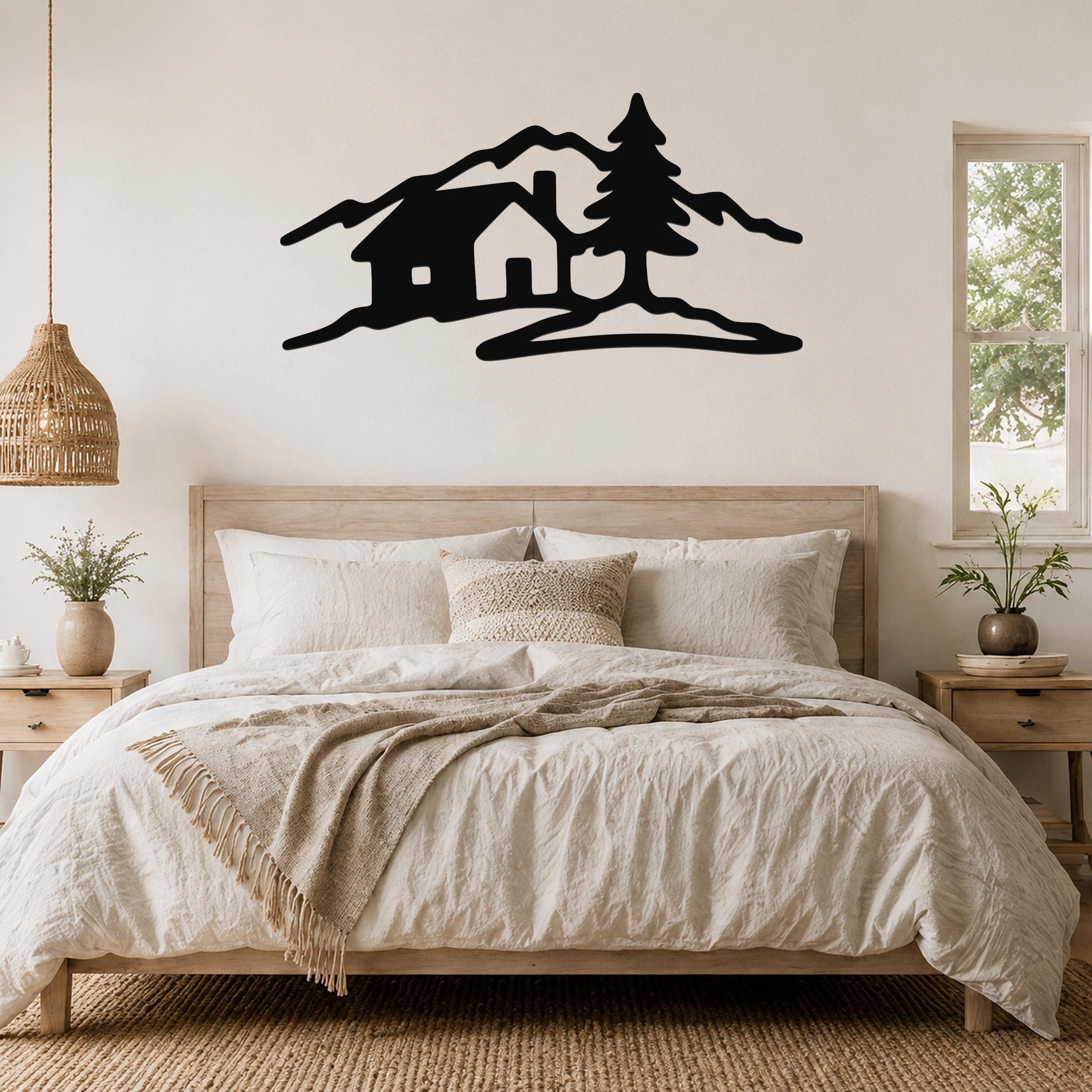 Black metal wall art silhouette of a cabin, pine tree, and mountains, mounted above a wooden bed in a bedroom.